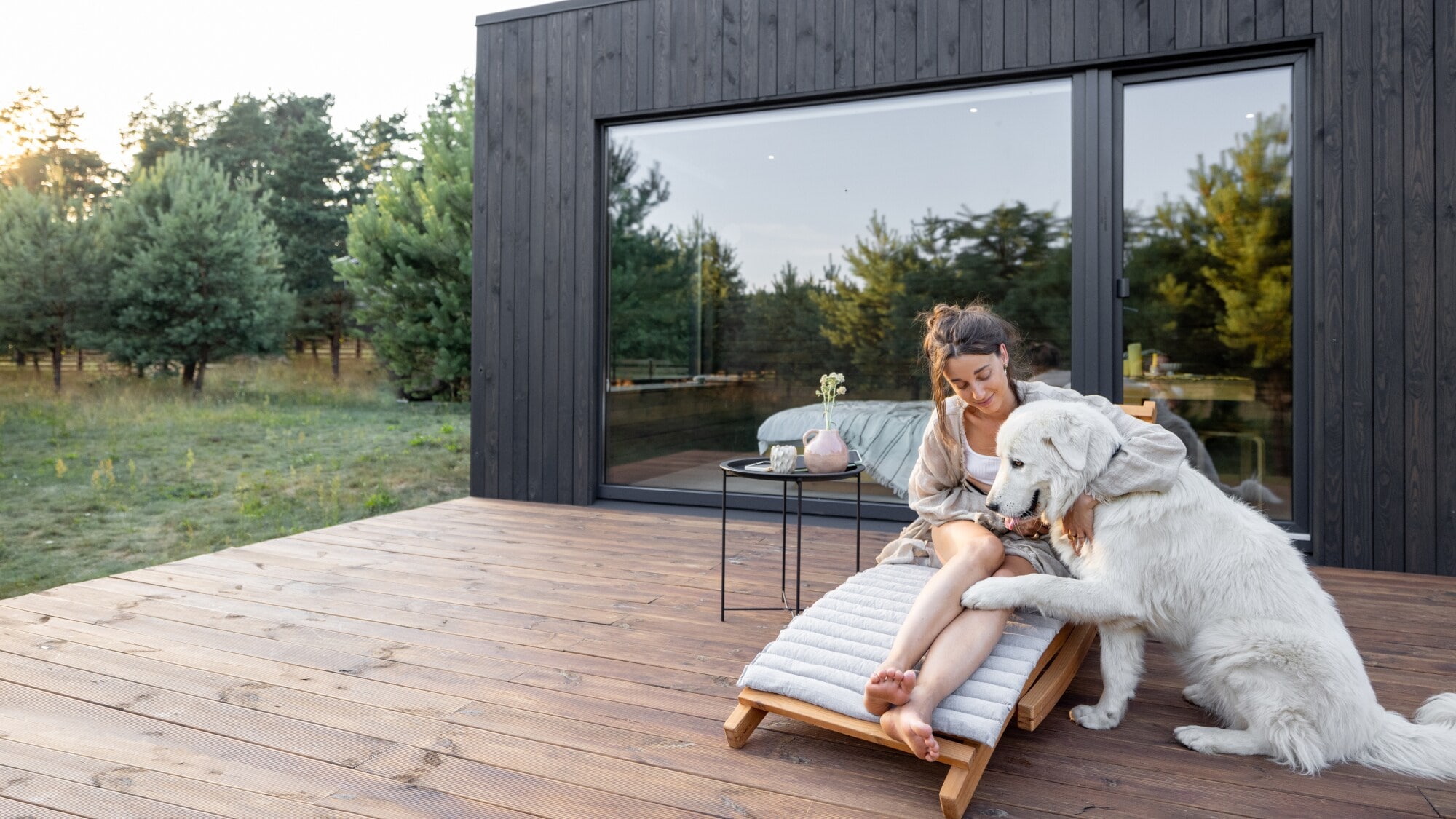 Wellness mit Hund Junge Frau sitzt im Freien auf einer Sonnenliege, neben sich einen großen weißen Hund.