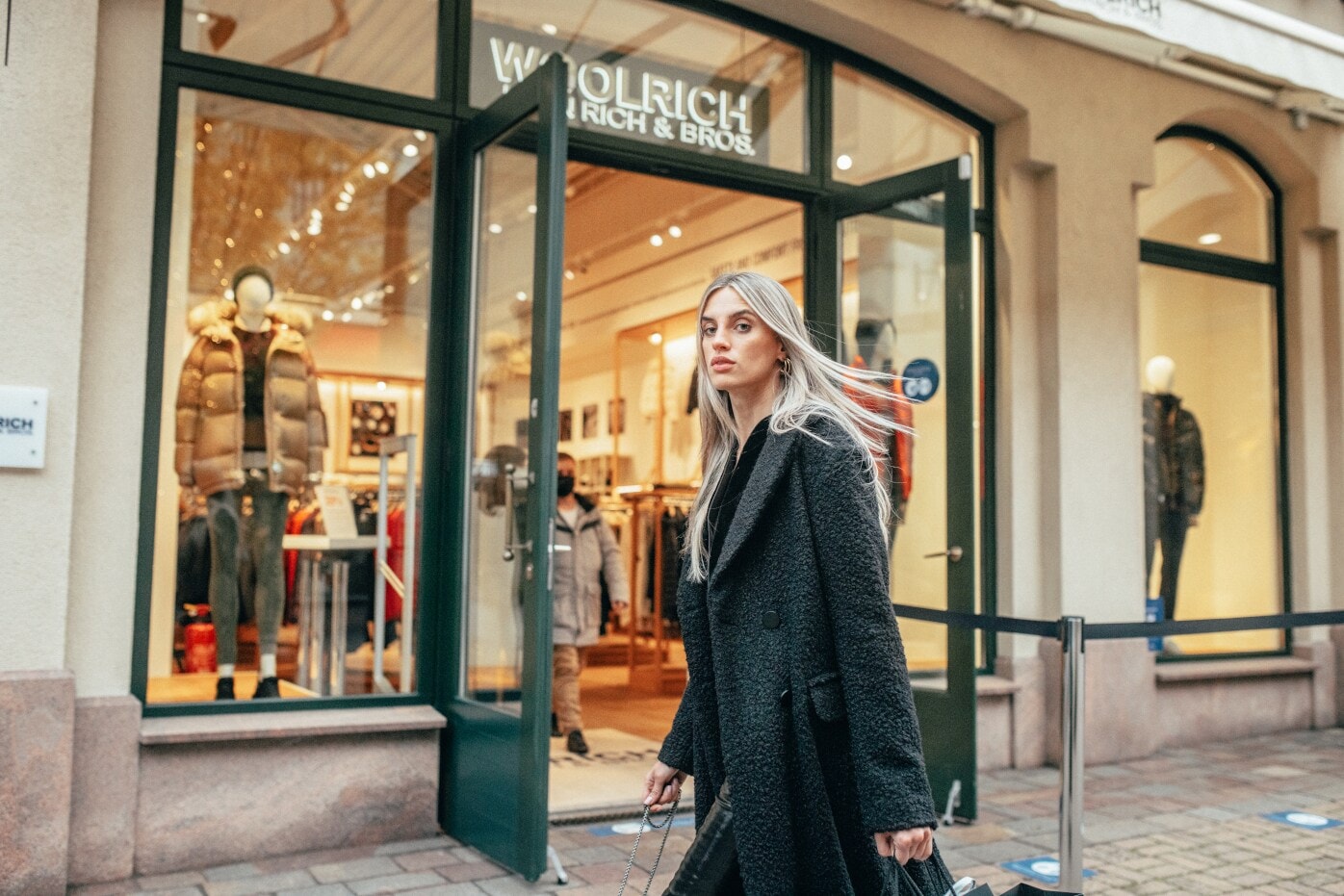 Eine Frau in langem schwarzen Mantel läuft an einem winterlichen Schaufenster vorbei Eine Frau in langem schwarzen Mantel läuft an einem winterlichen Schaufenster vorbei