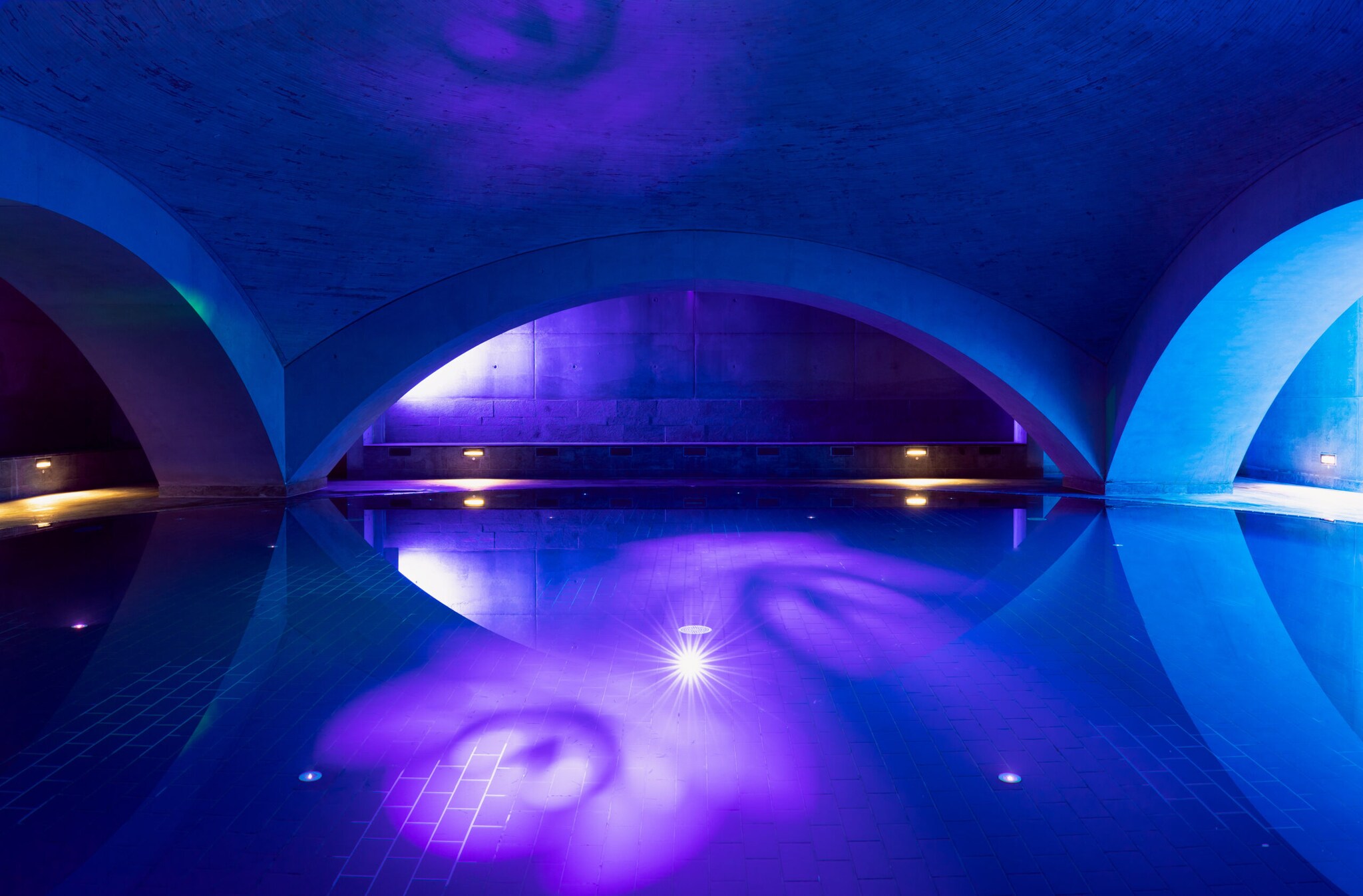 Minimalistisches Wasserbecken mit Rundbögen im blau-violetten Licht