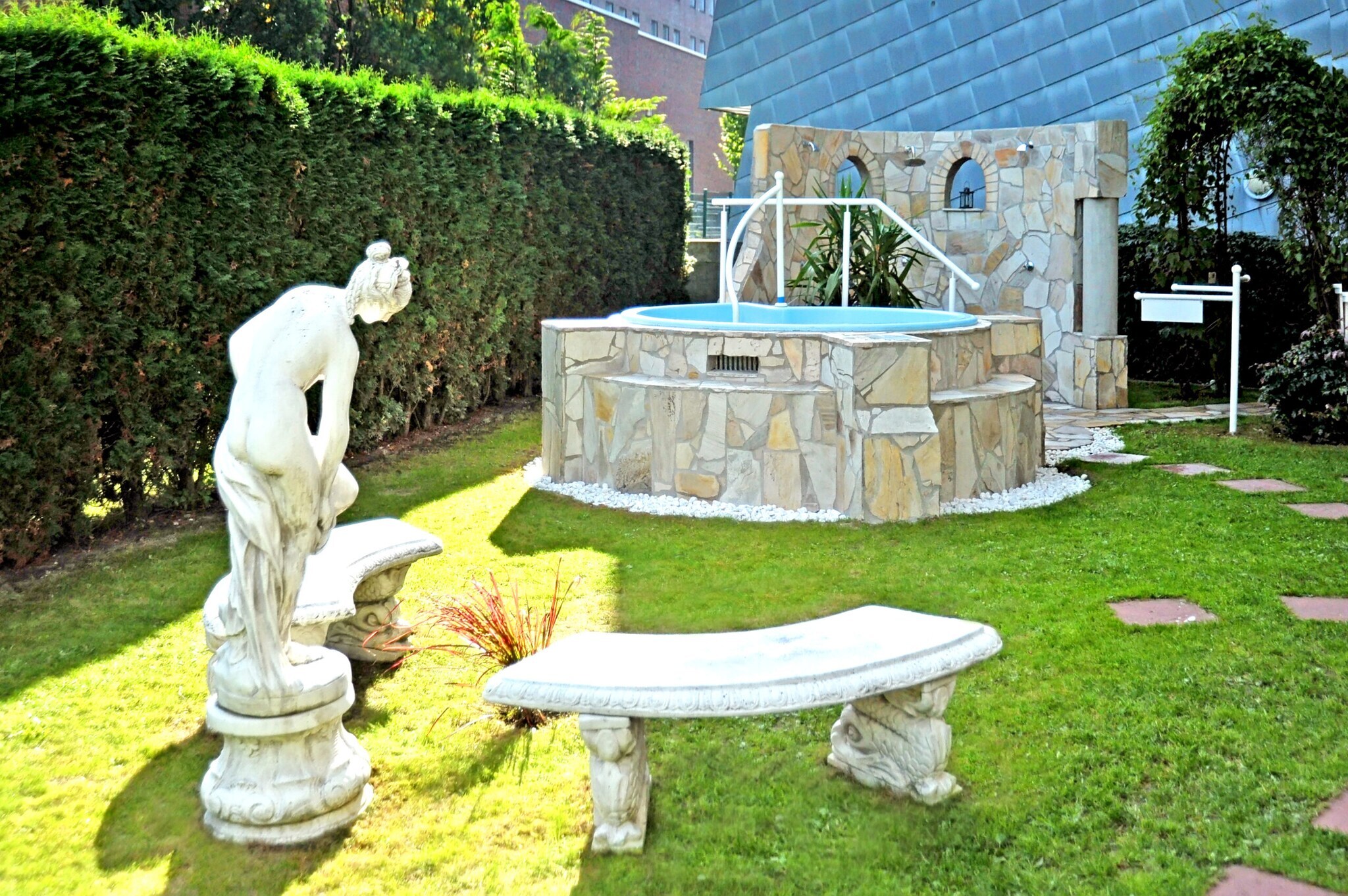 Whirlpool mit Mosaikfliesen in einem Garten mit einer Frauenstatue auf Sockel und zwei Bänken im antiken Design Whirlpool mit Mosaikfliesen in einem Garten mit einer Frauenstatue auf Sockel und zwei Bänken im antiken Design