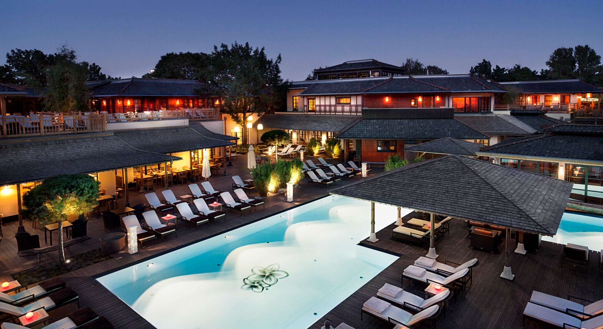 Beleuchteter Außenbereich einer Saunalandschaft mit Swimmingpool und Gebäuden im balinesischen Stil bei Dunkelheit Beleuchteter Außenbereich einer Saunalandschaft mit Swimmingpool und Gebäuden im balinesischen Stil bei Dunkelheit