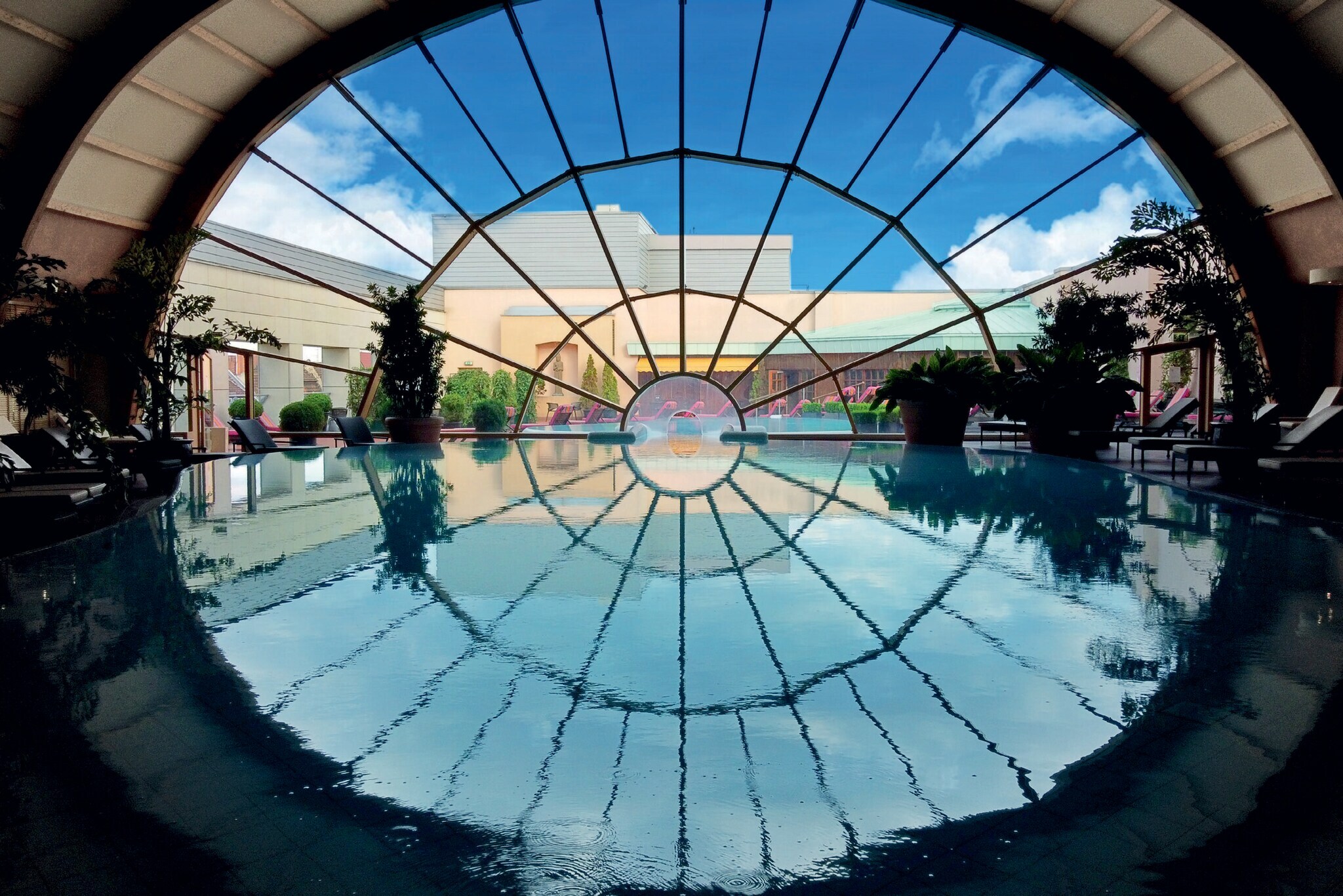 Ein großer Innenpool führt durch ein großes, rundes Panoramafenster in den Außenbereich mit Terrasse