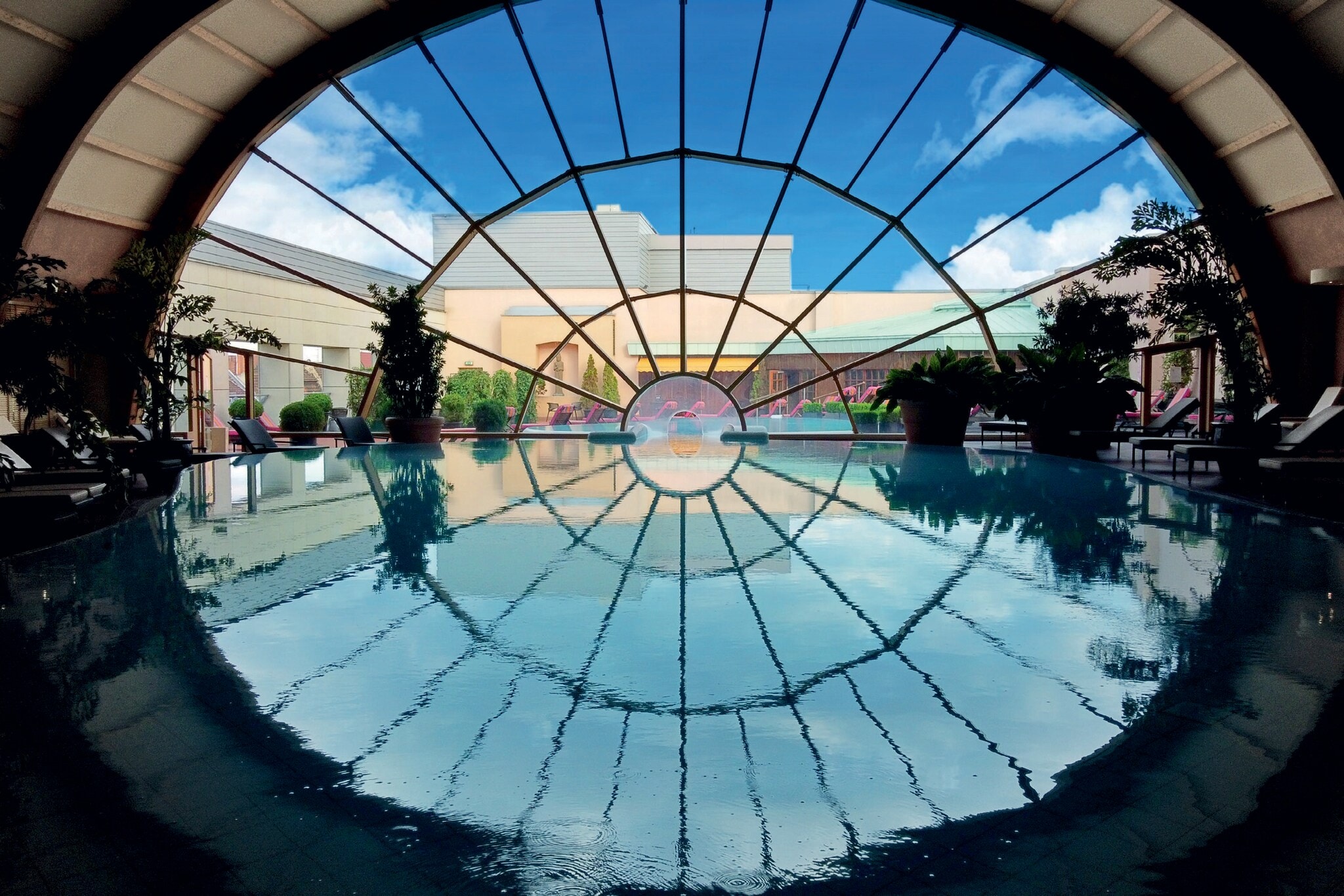 Ein großer Innenpool führt durch ein großes, rundes Panoramafenster in den Außenbereich mit Terrasse Ein großer Innenpool führt durch ein großes, rundes Panoramafenster in den Außenbereich mit Terrasse