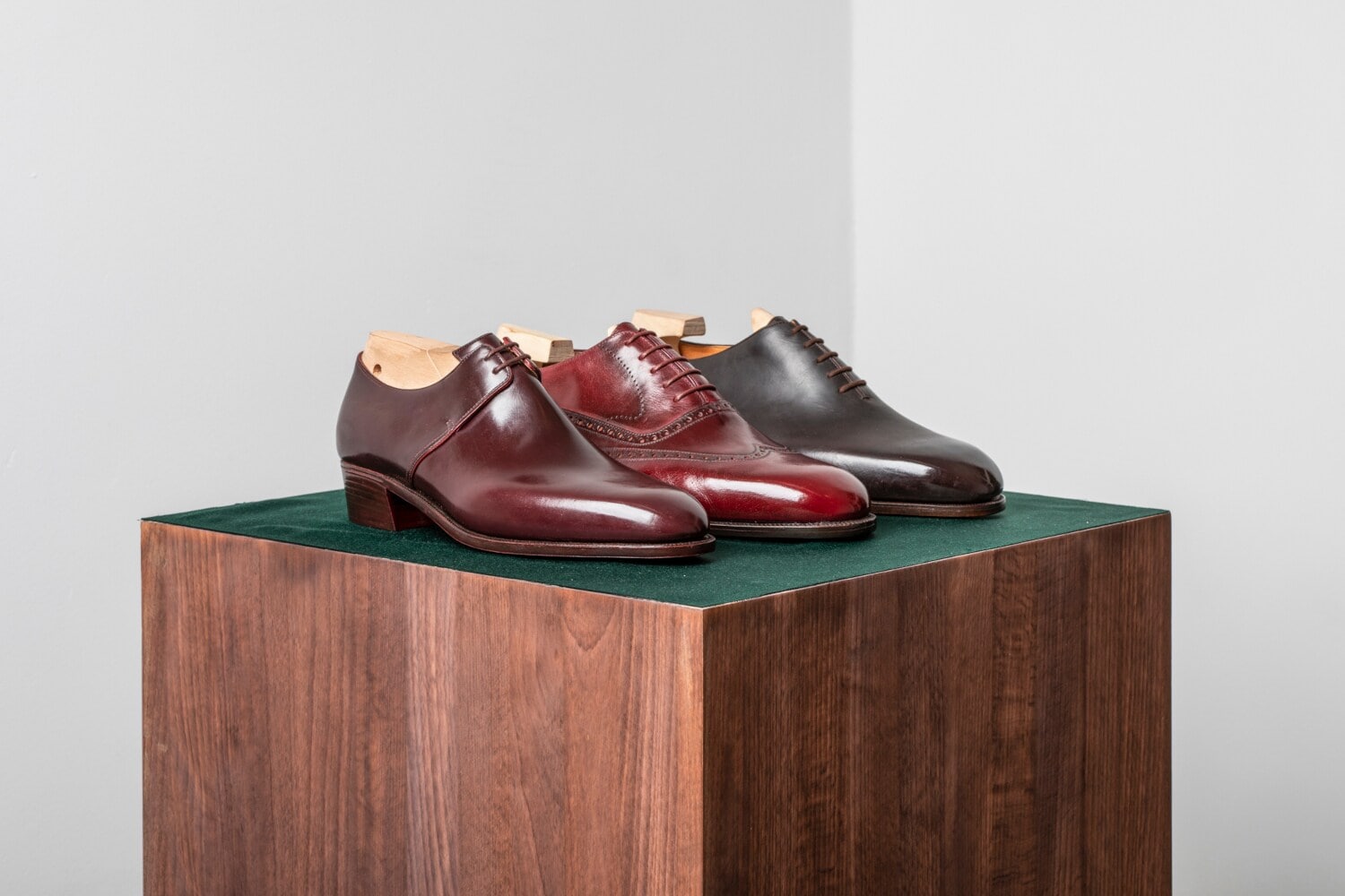 Drei verschiedenfarbige Lederschuhe auf einem Holzpodest vor weißem Hintergrund Drei verschiedenfarbige Lederschuhe auf einem Holzpodest vor weißem Hintergrund