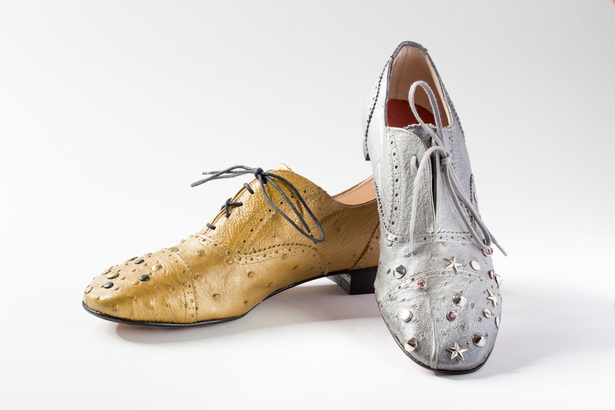 Ein goldener und ein silberner Schuh mit Nieten verziert vor einem weißen Hintergrund