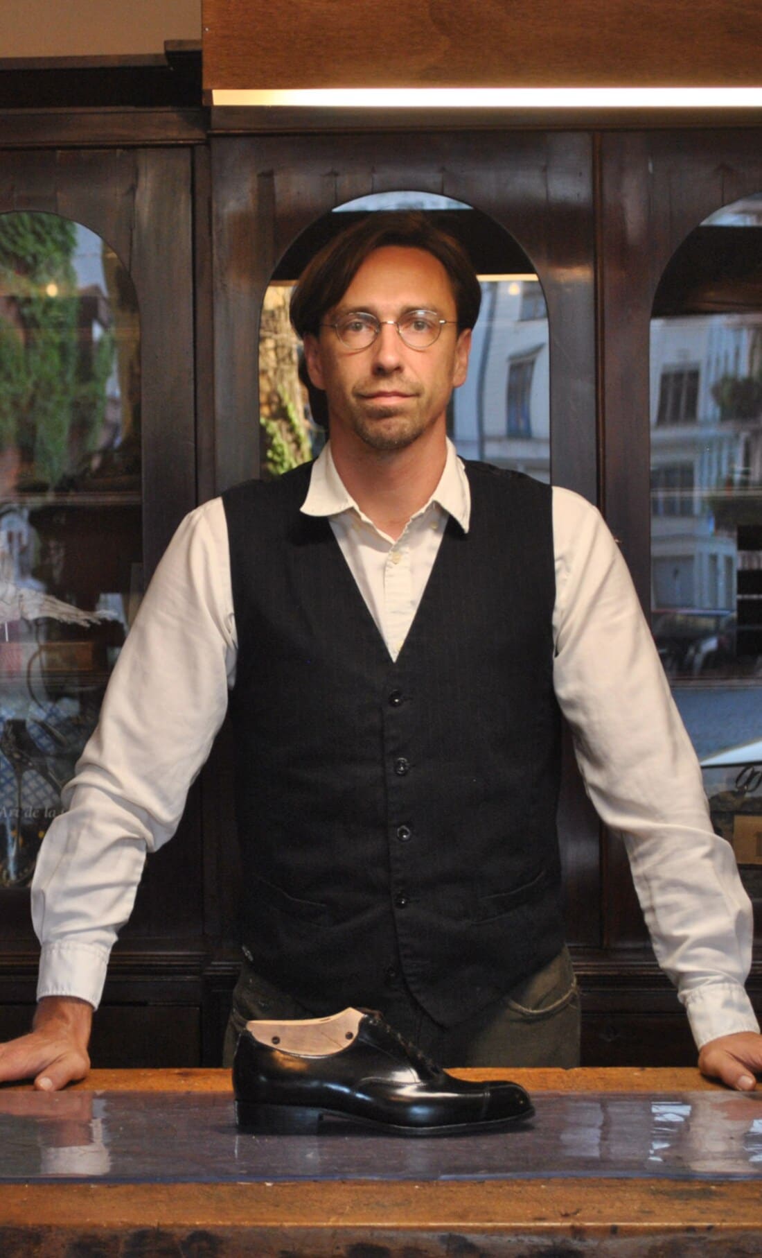 Mathieu Cortin steht hinter einem Tisch mit einem schwarzen, glänzenden Lederschuh darauf Mathieu Cortin steht hinter einem Tisch mit einem schwarzen, glänzenden Lederschuh darauf