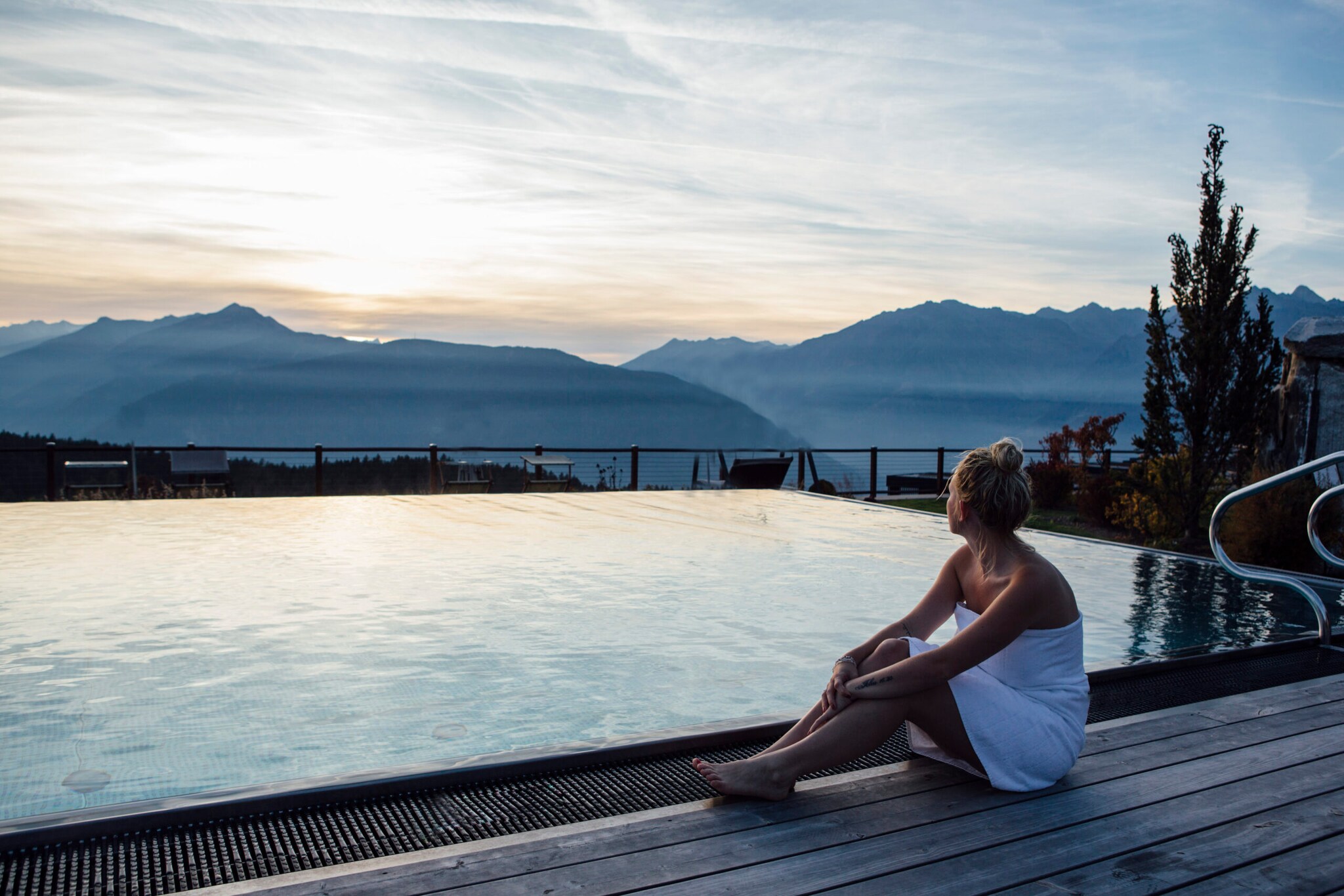 Eine Frau mit umwickelten Handtuch sitzt an einem Outdoor-Pool mit Blick auf die Berge in der Dämmerung Eine Frau mit umwickelten Handtuch sitzt an einem Outdoor-Pool mit Blick auf die Berge in der Dämmerung