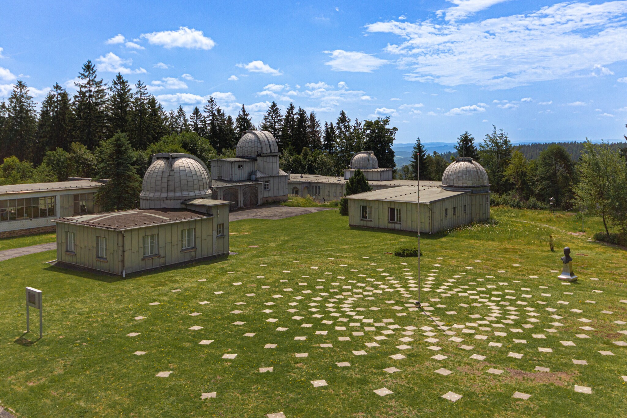 Gelände der Sternwarte Sonneberg, auf dem sich mehrere Gebäude mit Kuppeln befinden, daneben eine Installation mit Markierungssteinen, die sich kreisförmig am Boden um eine Stange anordnen