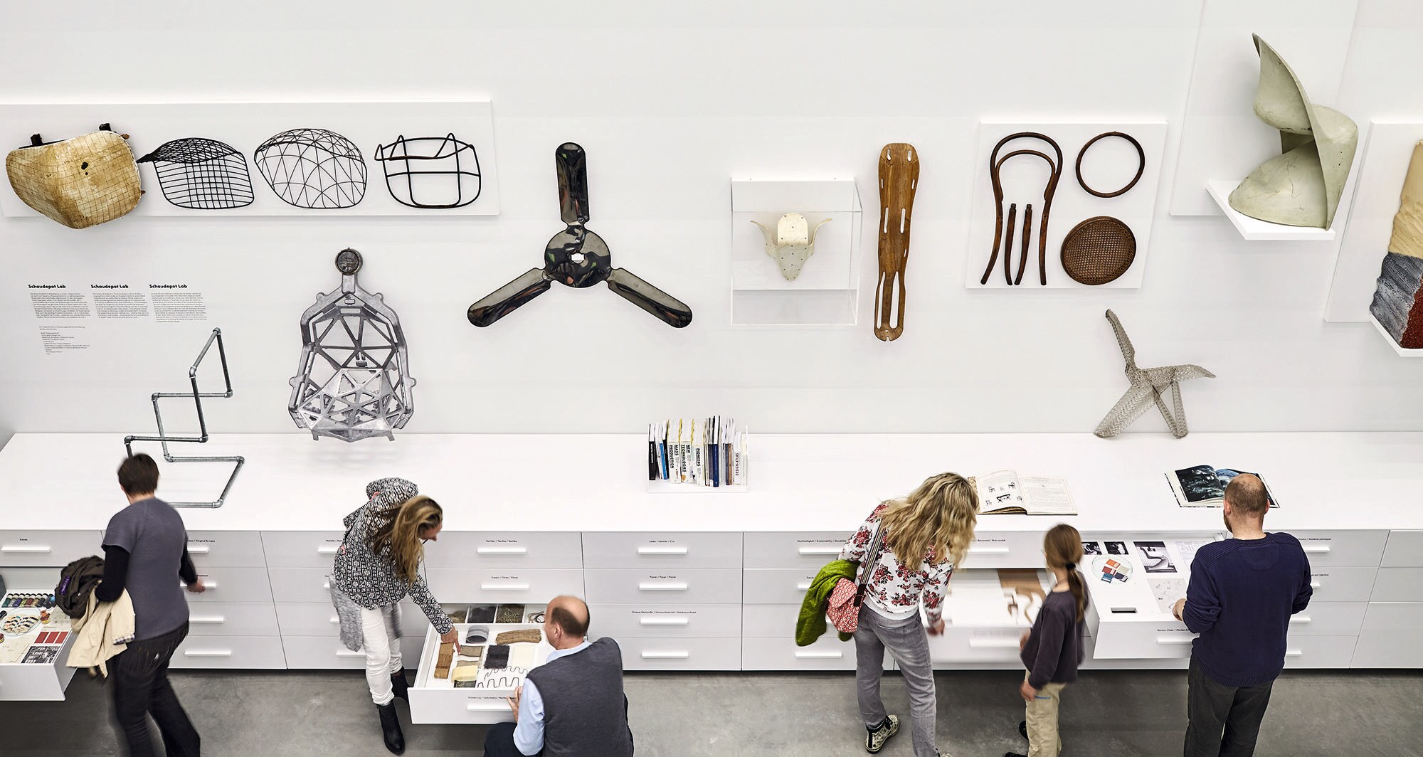 Ein Raum mit Ausstellungsstücken und Menschen, die diese betrachten und anfassen, aus der Vogelperspektive