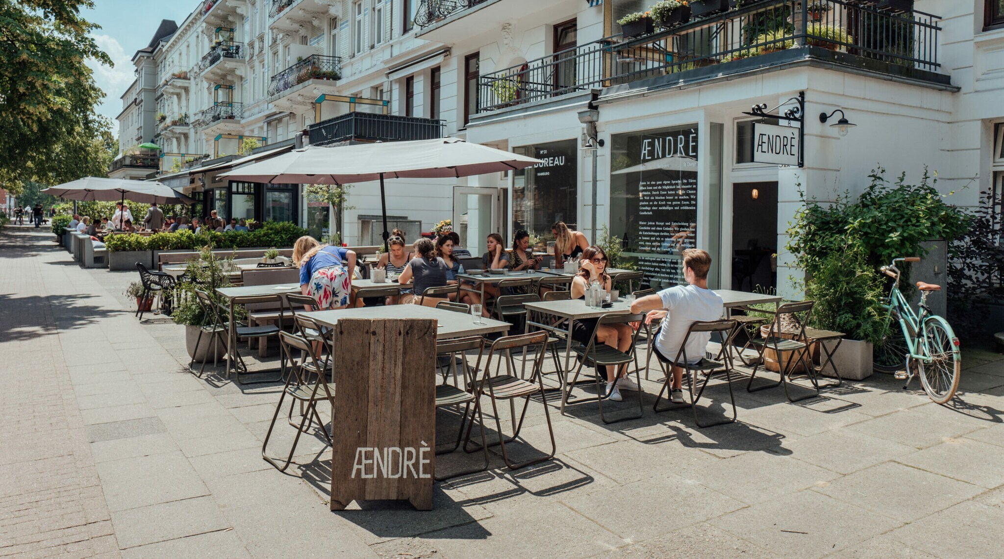 Außenaufnahme des Cafés Aendre mit Gästen auf der bestuhlten Terrasse bei Sonnenschein