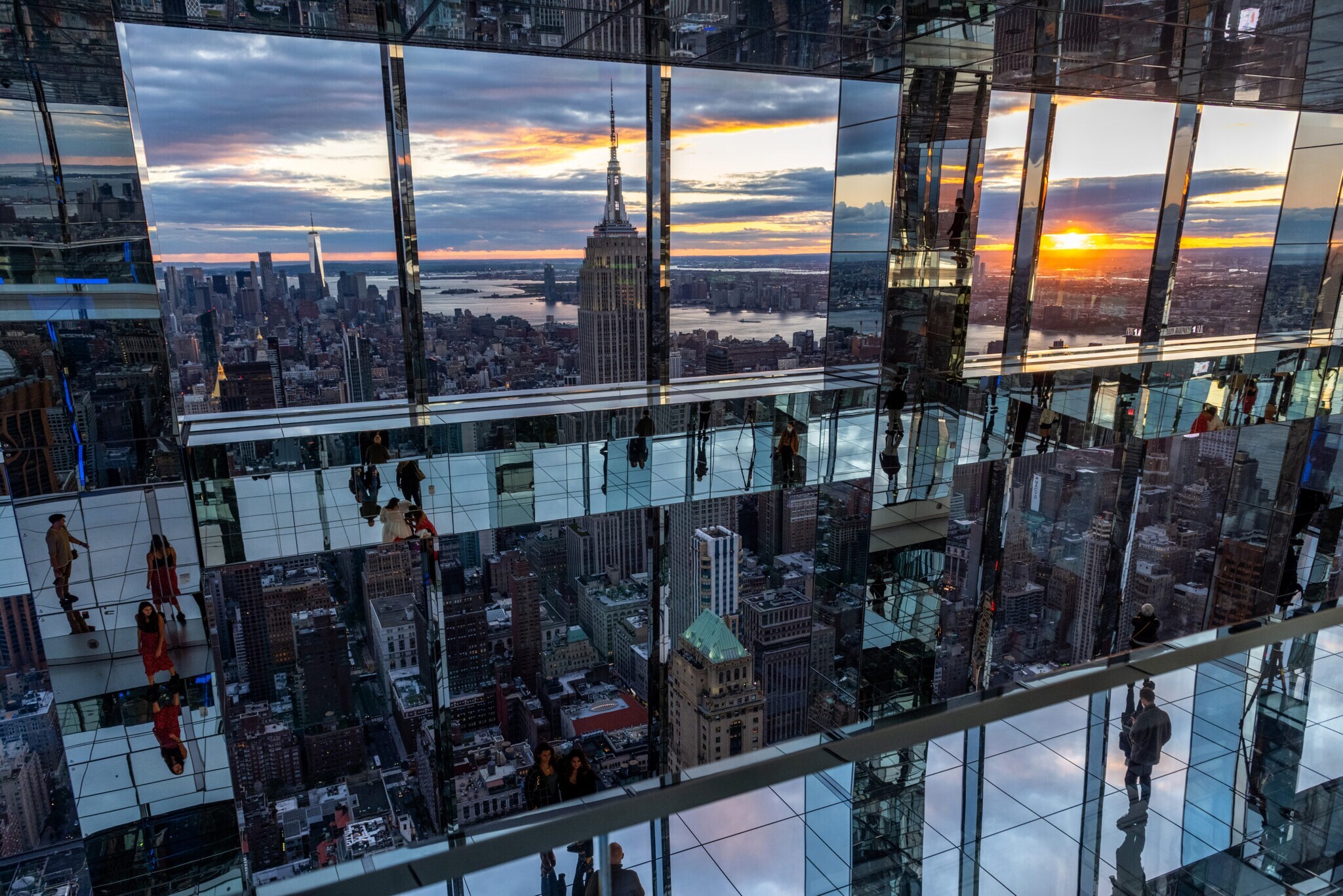 Besucher laufen über eine gläserne Aussichtsplattform in Manhattan mit Blick auf das Empire State Building