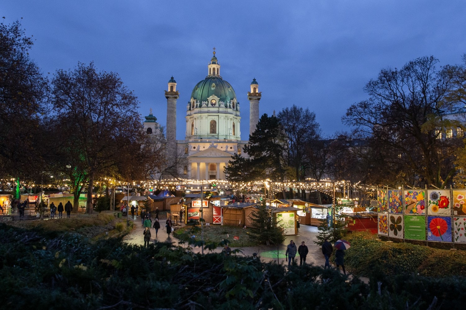 Beleuchteter Weihnachtsmarkt mit Verkaufsständen vor der Karlskirche in Wien bei Nacht Beleuchteter Weihnachtsmarkt mit Verkaufsständen vor der Karlskirche in Wien bei Nacht