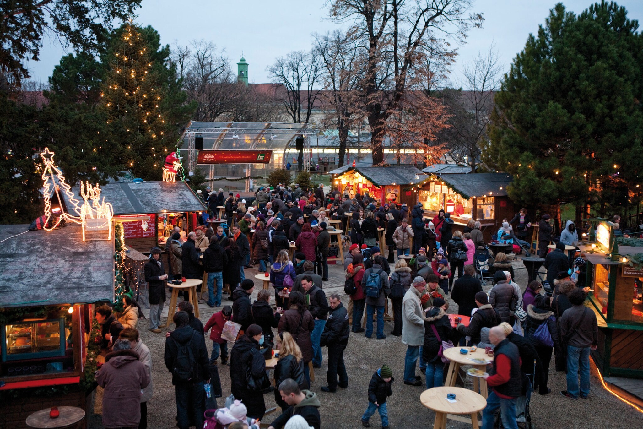Weihnachtsmarkt mit Menschenansammlung umgeben von Verkaufsständen in der Dämmerung
