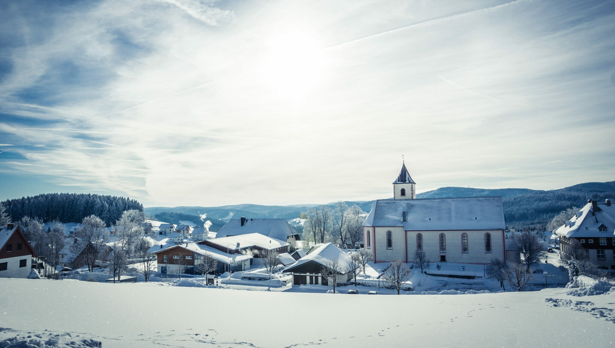Ein eingeschneites Dorf im Sonnenschein, im Hintergrund Berge
