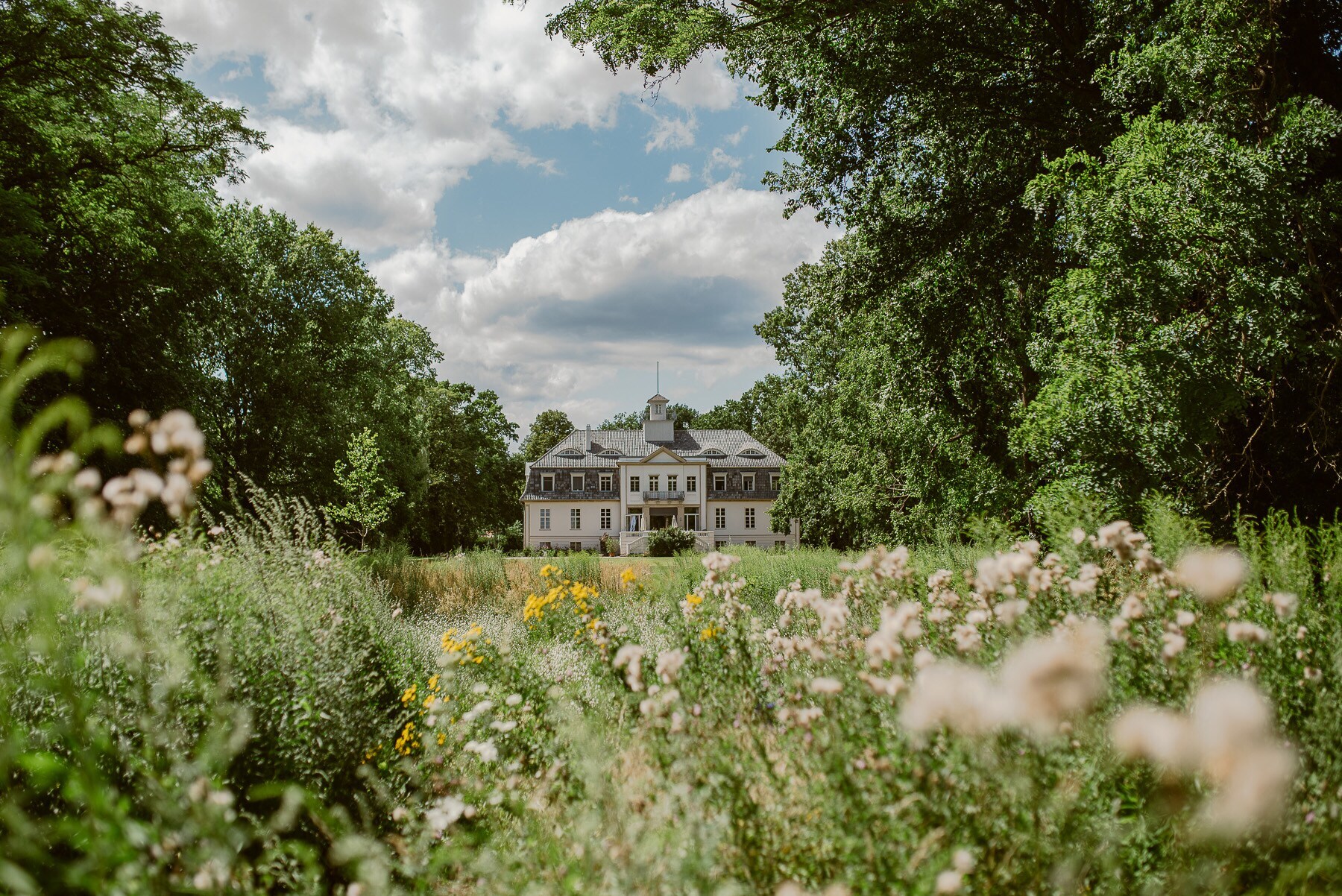 Ein altes aber restauriertes Schloss inmitten eines grünen Parks mit alten Bäumen und Wildblumen