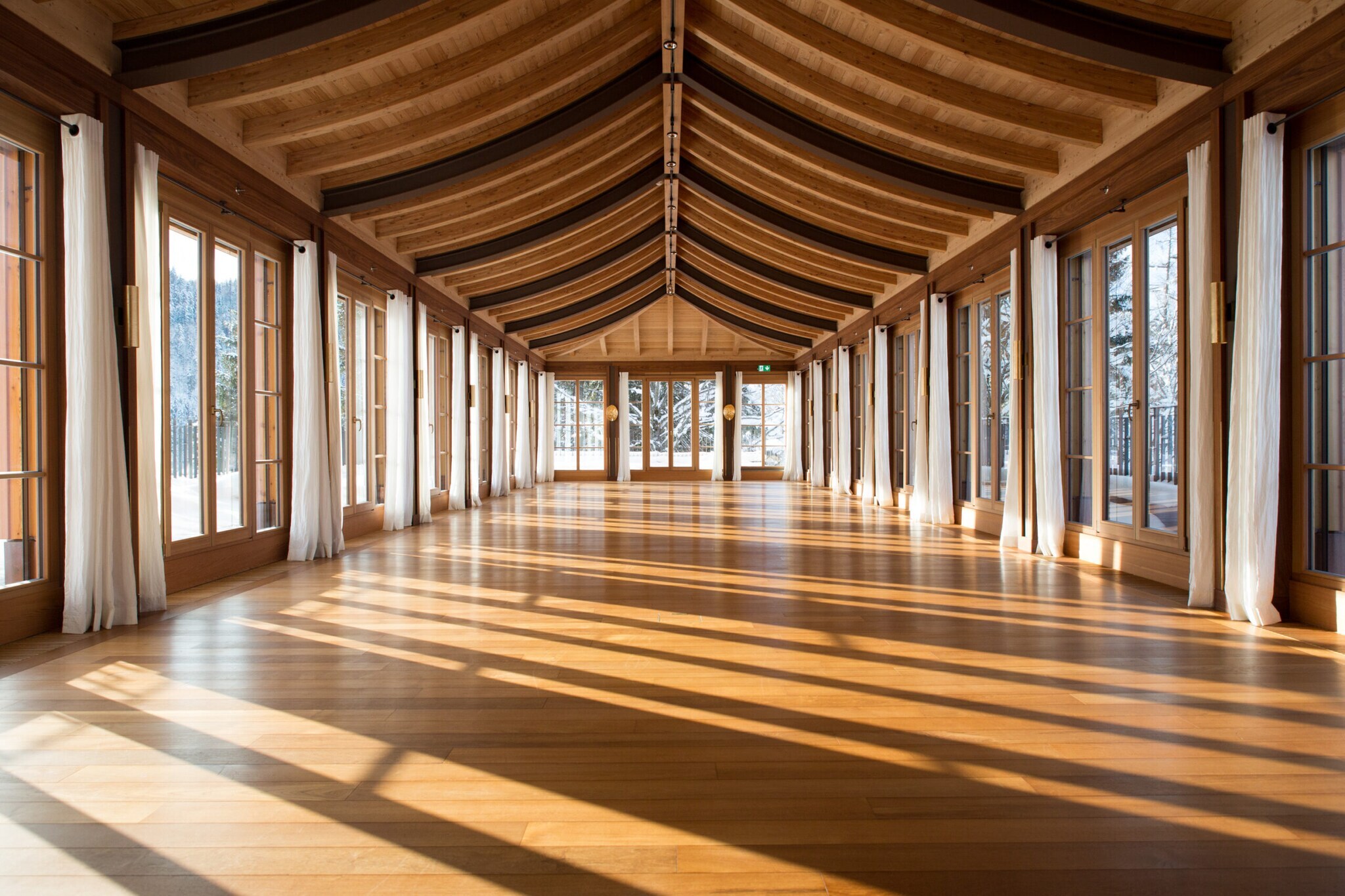 Ein großer, lichtdurchfluteter Raum aus Holz mit bodentiefen Fenstern und einem fernöstlichen Walmdach