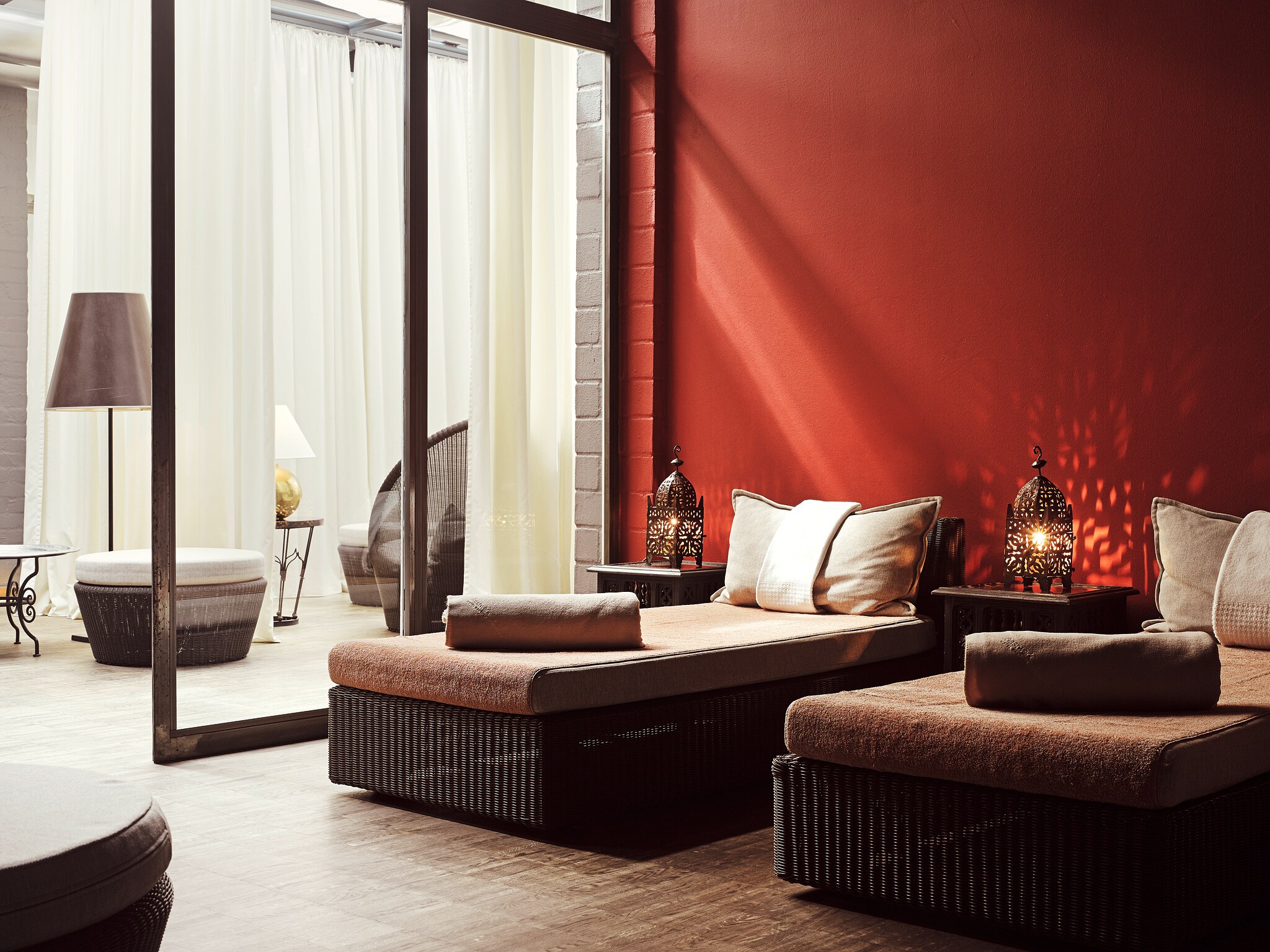 Innenraum mit zwei gepolsterten Liegen vor einer roten Wand und edlen Accessoires Innenraum mit zwei gepolsterten Liegen vor einer roten Wand und edlen Accessoires