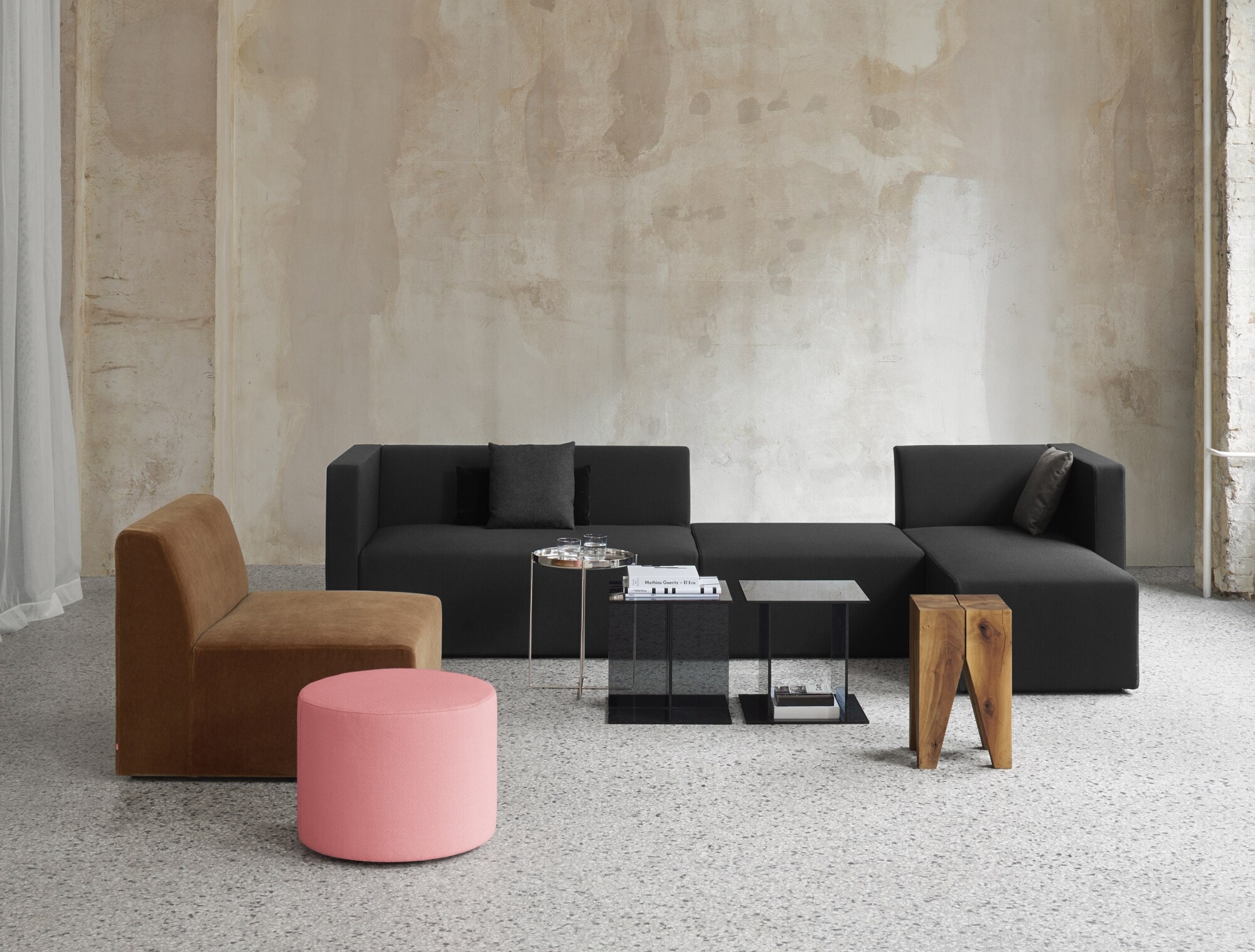 Sitzgruppe aus minimalistischen Polstermöbeln und Beistelltischen in einem hellen Raum mit Betonwand Sitzgruppe aus minimalistischen Polstermöbeln und Beistelltischen in einem hellen Raum mit Betonwand