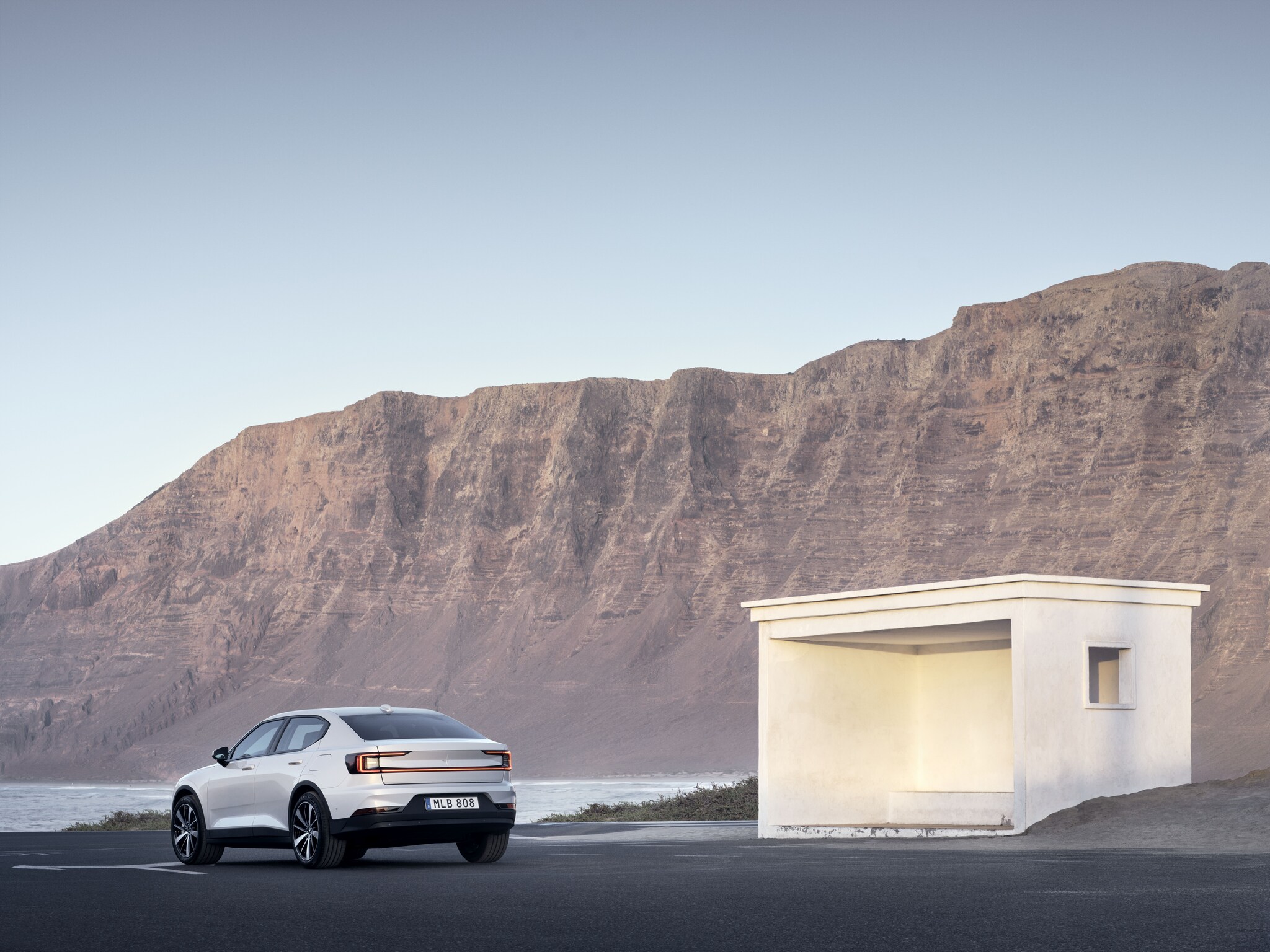 Der Polestar 2 passiert ein weißes Häuschen vor einem Felsmassiv.