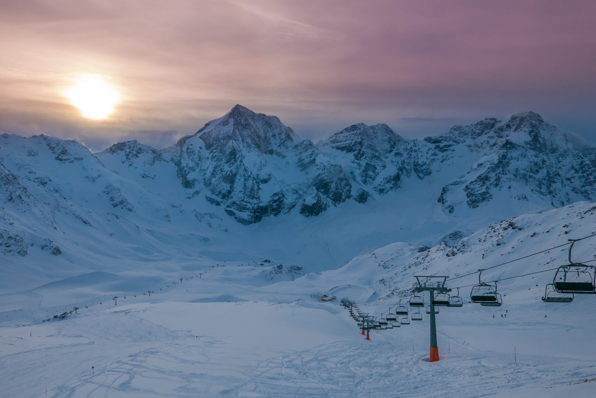 Seilbahn, Schnee und Berge. Im Hintergrund ein Sonnenuntergang