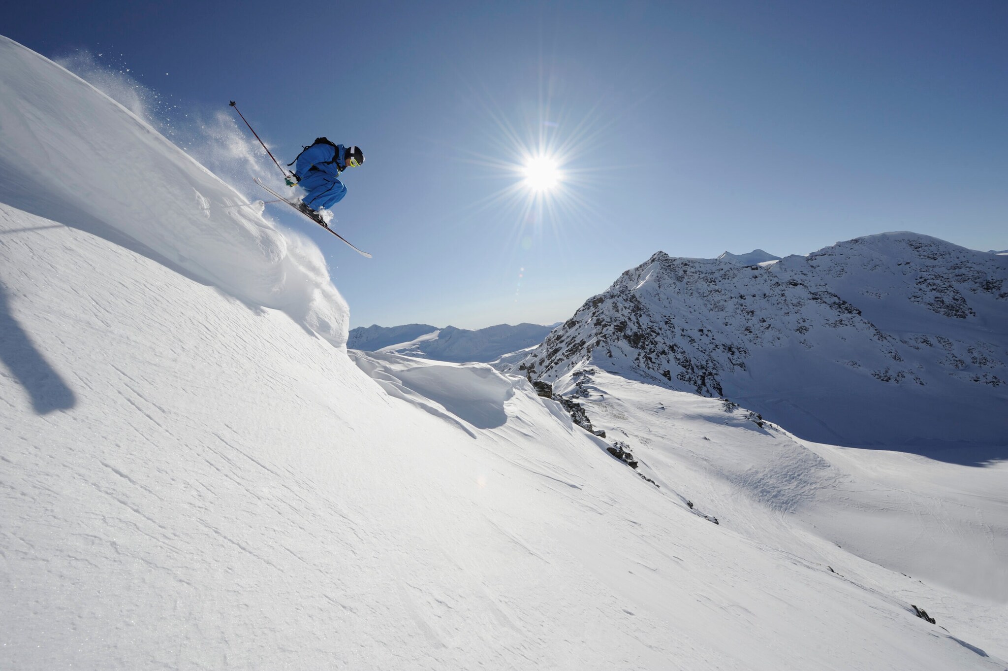 Skifahrer:in springt von einer Klippe, Sonne und Schnee Skifahrer:in springt von einer Klippe, Sonne und Schnee
