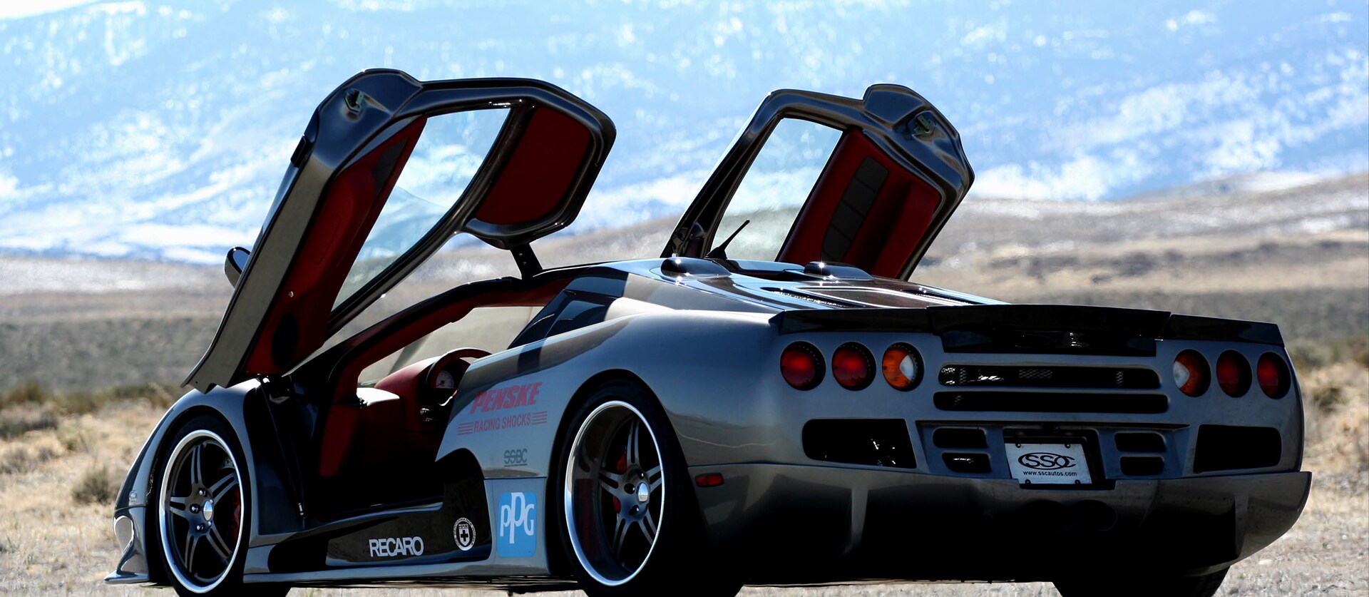 Der SSC Ultimate Aero TT mit offenen Flügeltüren, im Hintergrund eine Landschaft.