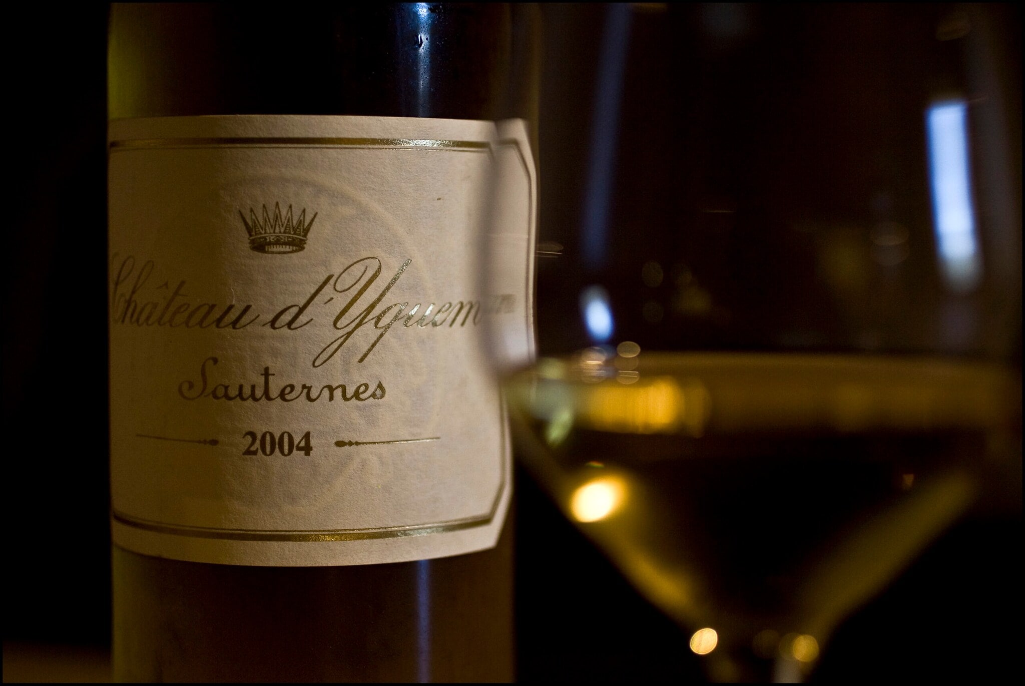 Nahaufnahme eines Weinetiketts mit einem gefüllten Glas Weißwein im Vordergrund Nahaufnahme eines Weinetiketts mit einem gefüllten Glas Weißwein im Vordergrund