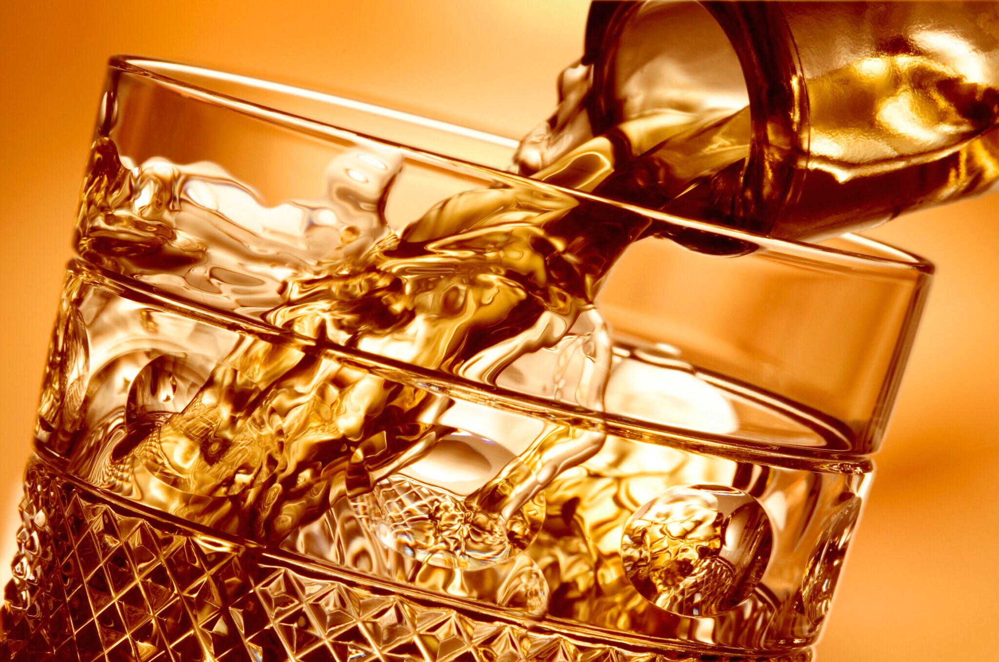 In ein Whiskyglas wird Flüssigkeit aus einem Flaschenhals gegossen, Nahaufnahme mit goldener Bildtonung