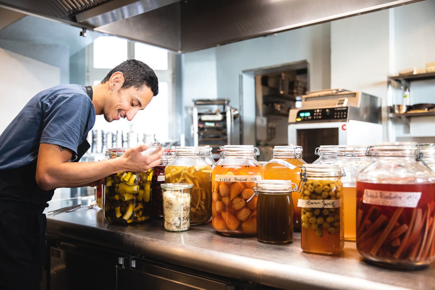 Ein Mann steht an einer Küchentheke, auf der verschiedene Einmachgläser mit Früchten und Gemüse aufgereiht sind