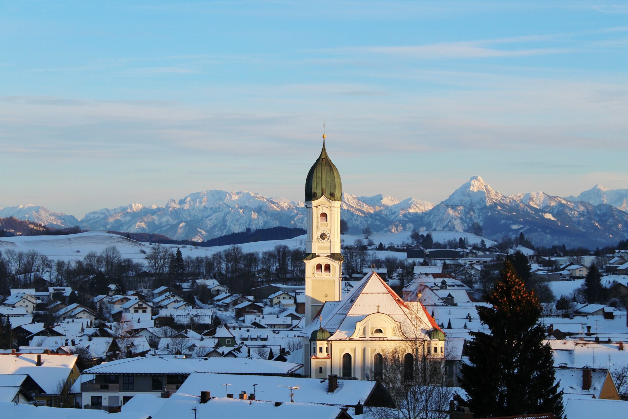 Schneebedeckter Ort mit weißer Kirche vor Alpenpanorama in der Dämmerung Schneebedeckter Ort mit weißer Kirche vor Alpenpanorama in der Dämmerung
