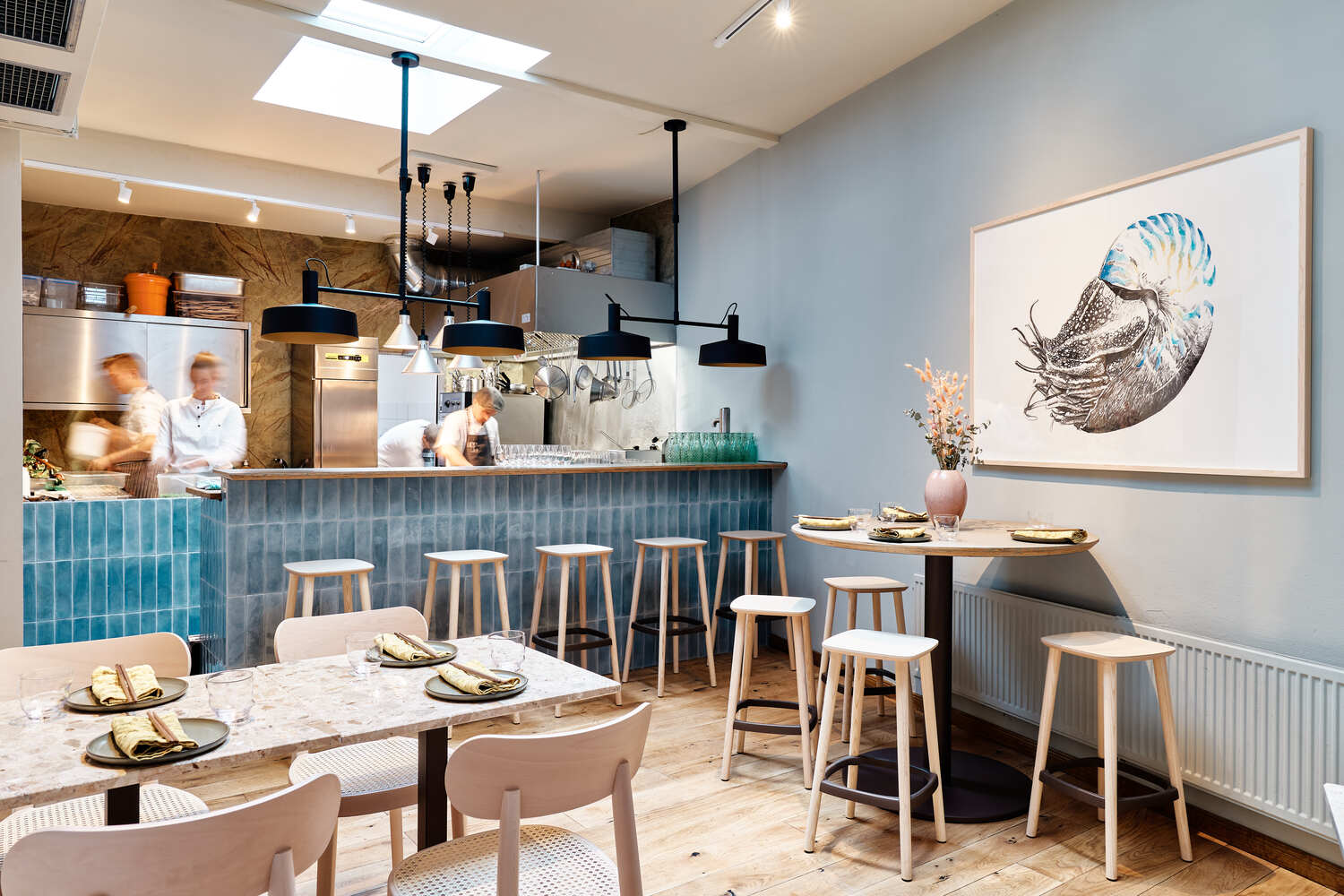 Austernbar mit Holzstühlen und einem blau gekachelten Tresen, hinter dem Köche Speisen zubereiten