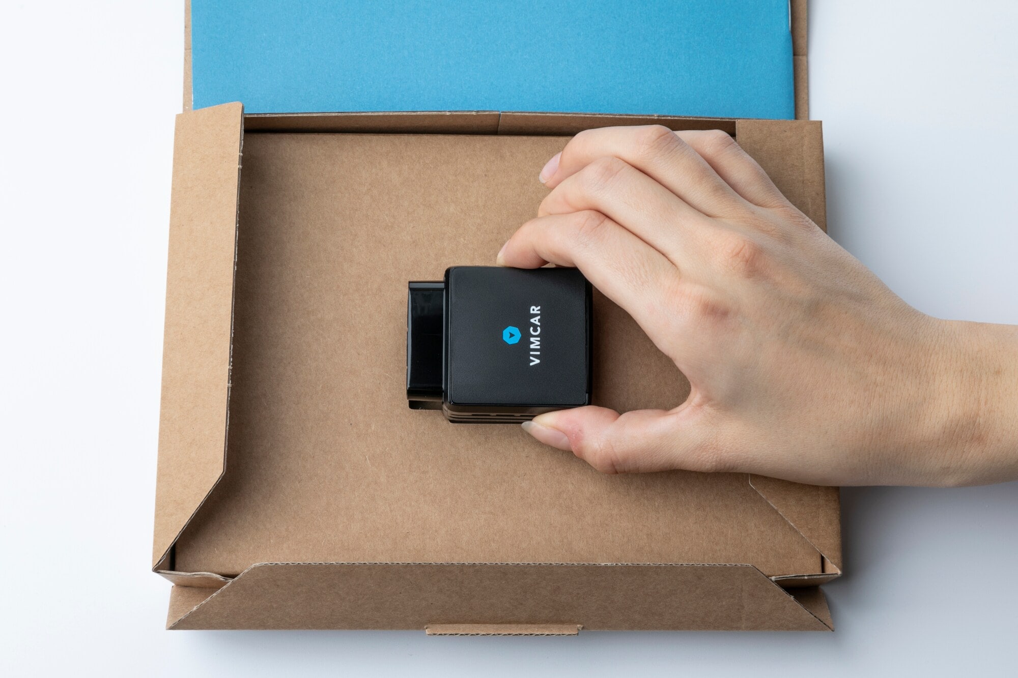 Ein kleines schwarzes OBD-2-Modul liegt auf einem braunen Karton und wird von einer Hand umfasst Ein kleines schwarzes OBD-2-Modul liegt auf einem braunen Karton und wird von einer Hand umfasst