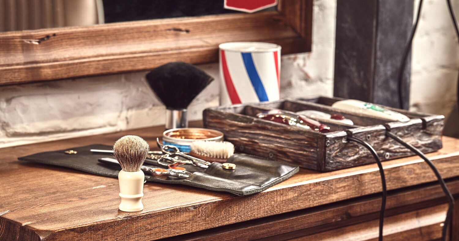 Auf einer Holzkommode unter einem Spiegel liegen klassische Barbertools wie Rasiermesser- und Pinsel