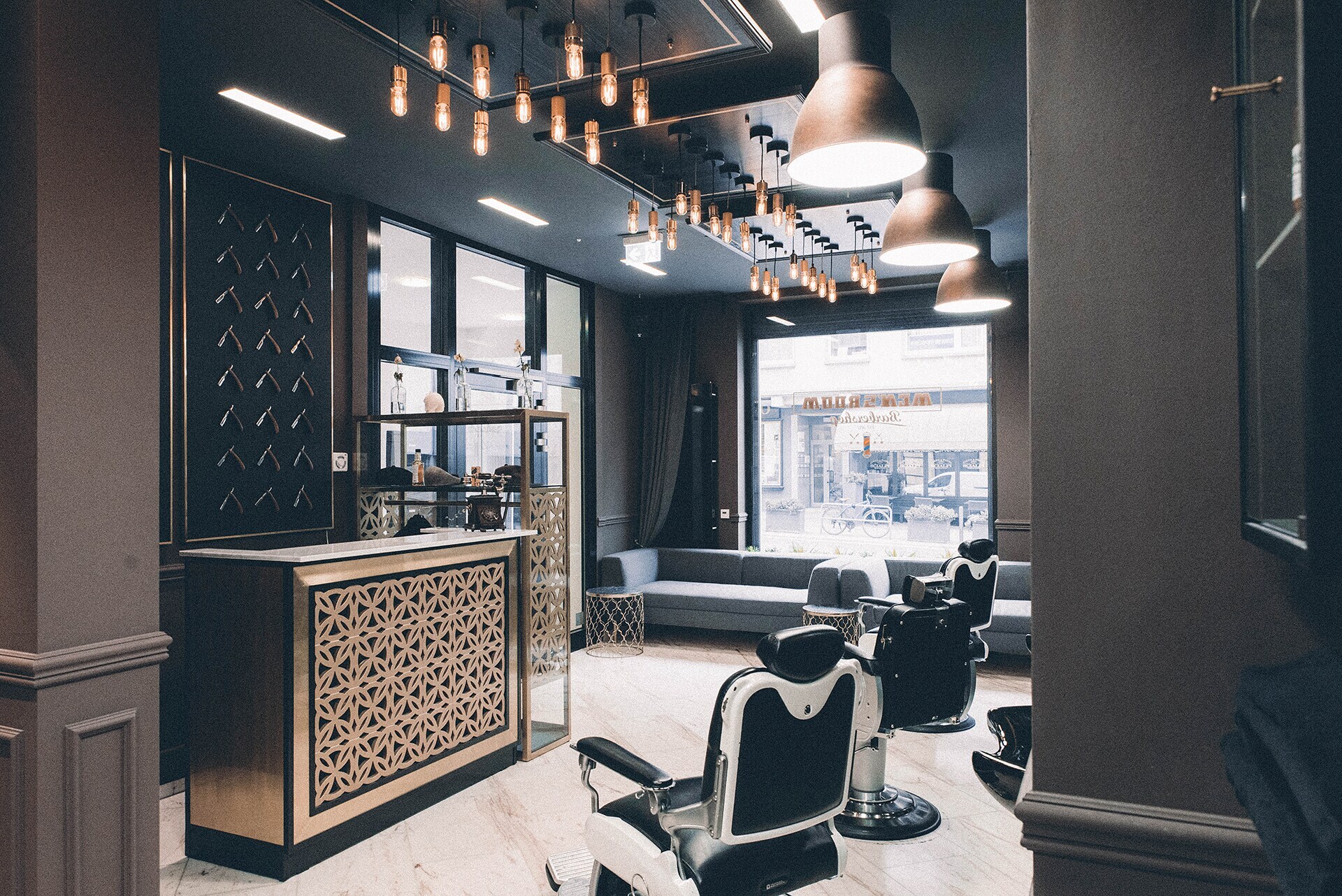 Das Interieur eines modernen Barbershops mit einem Messing verkleideten Tresen, Friseurstühlen aus Leder und einem dunkel gehaltenen cleanen Ambiente