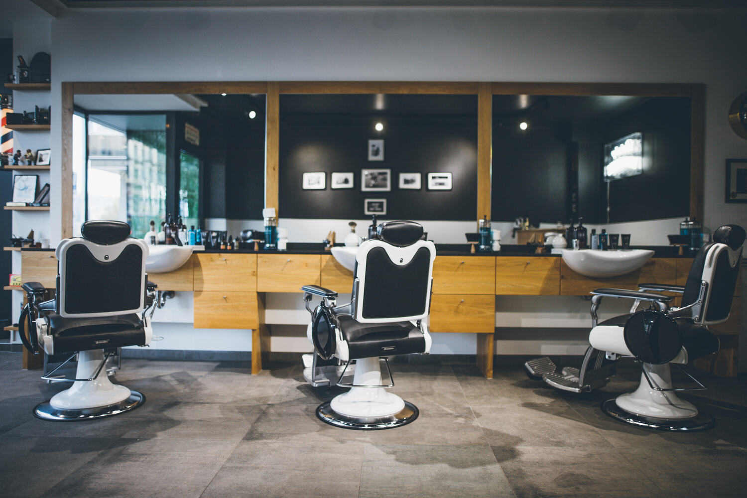 Drei moderne Friseursessel vor Waschbecken und Spiegel in einem Barbershop
