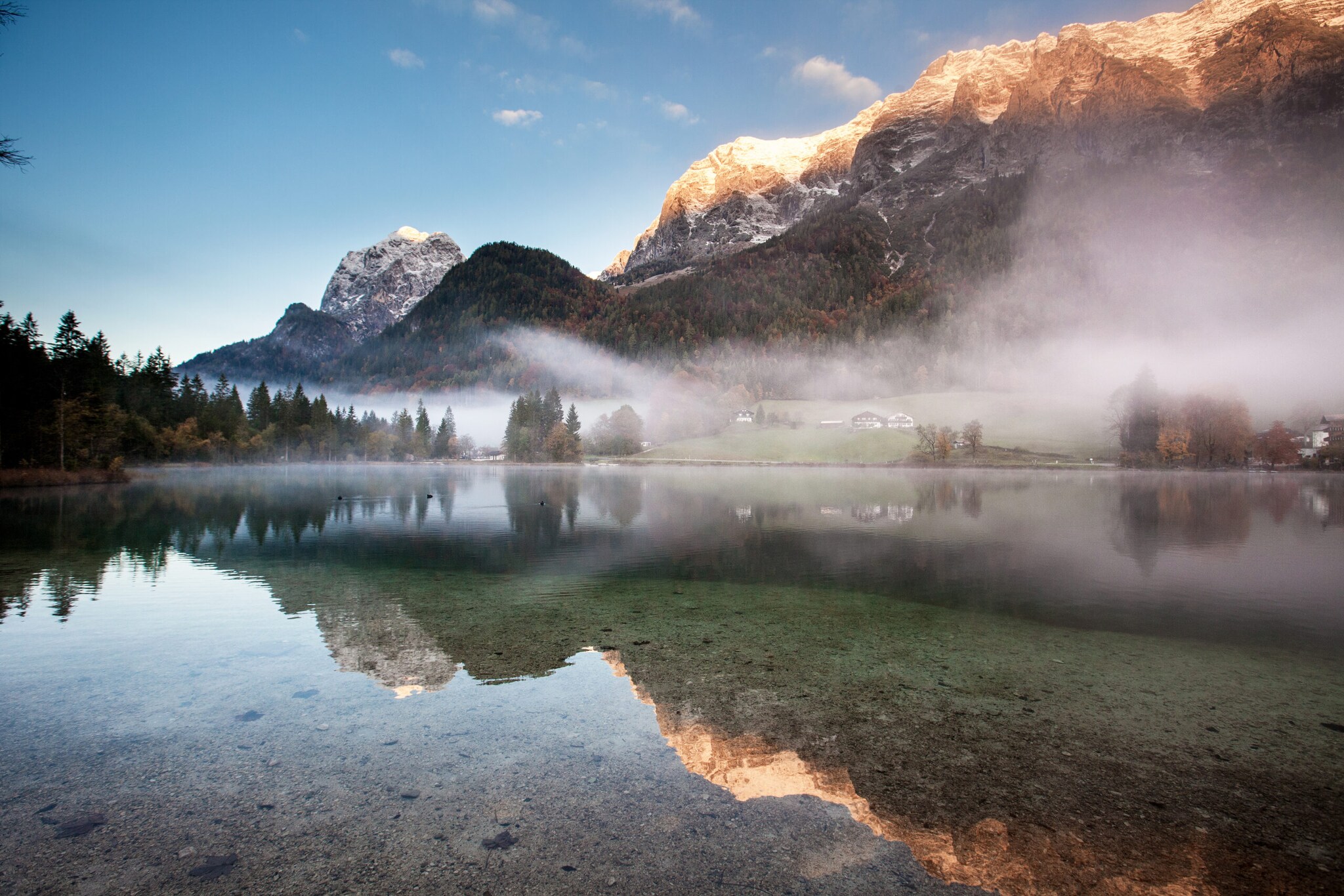 Ein See mit glasklarem Wasser über dem Nebelschwaden liegen vor Bergpanorama in der Dämmerung Ein See mit glasklarem Wasser über dem Nebelschwaden liegen vor Bergpanorama in der Dämmerung