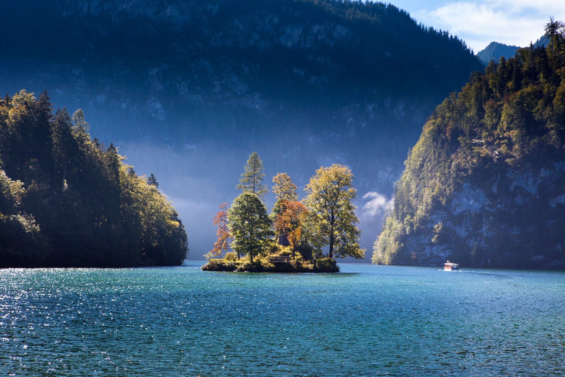 Ein großer See mit einer Insel mit herbstlichen Laubbäumen, eingebettet von riesigen Felswänden Ein großer See mit einer Insel mit herbstlichen Laubbäumen, eingebettet von riesigen Felswänden