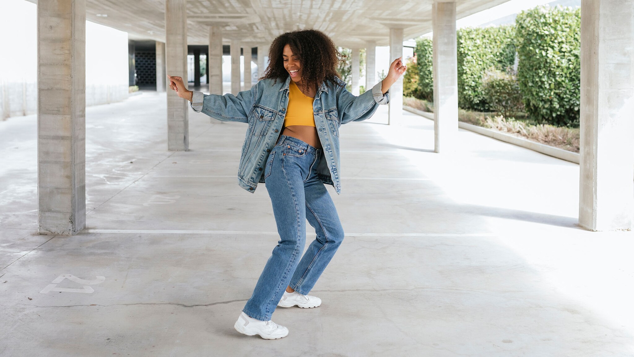 Eine junge Frau in Jeanskleidung tanzt in einem leeren Parkhaus.