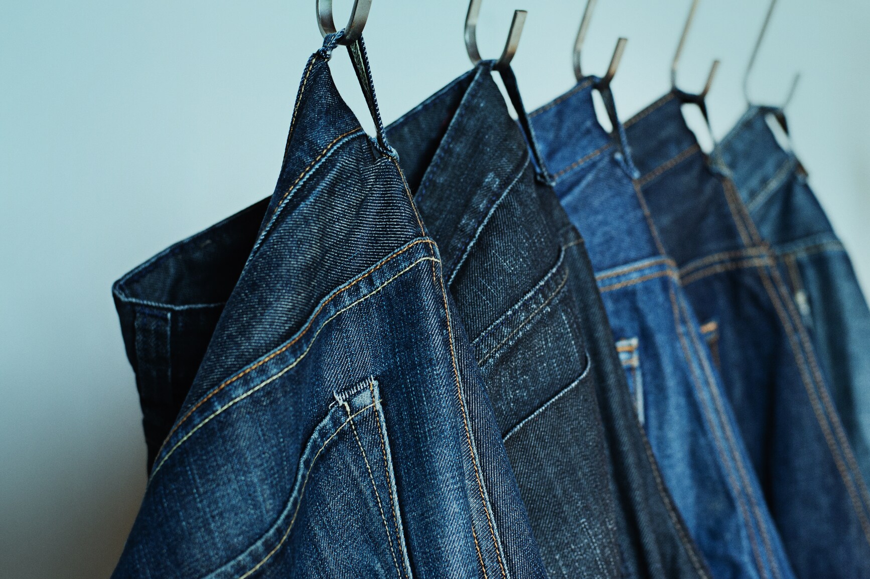 Jeanshosen in unterschiedlichen Waschungen nebenenander an Haken aufgehängt.