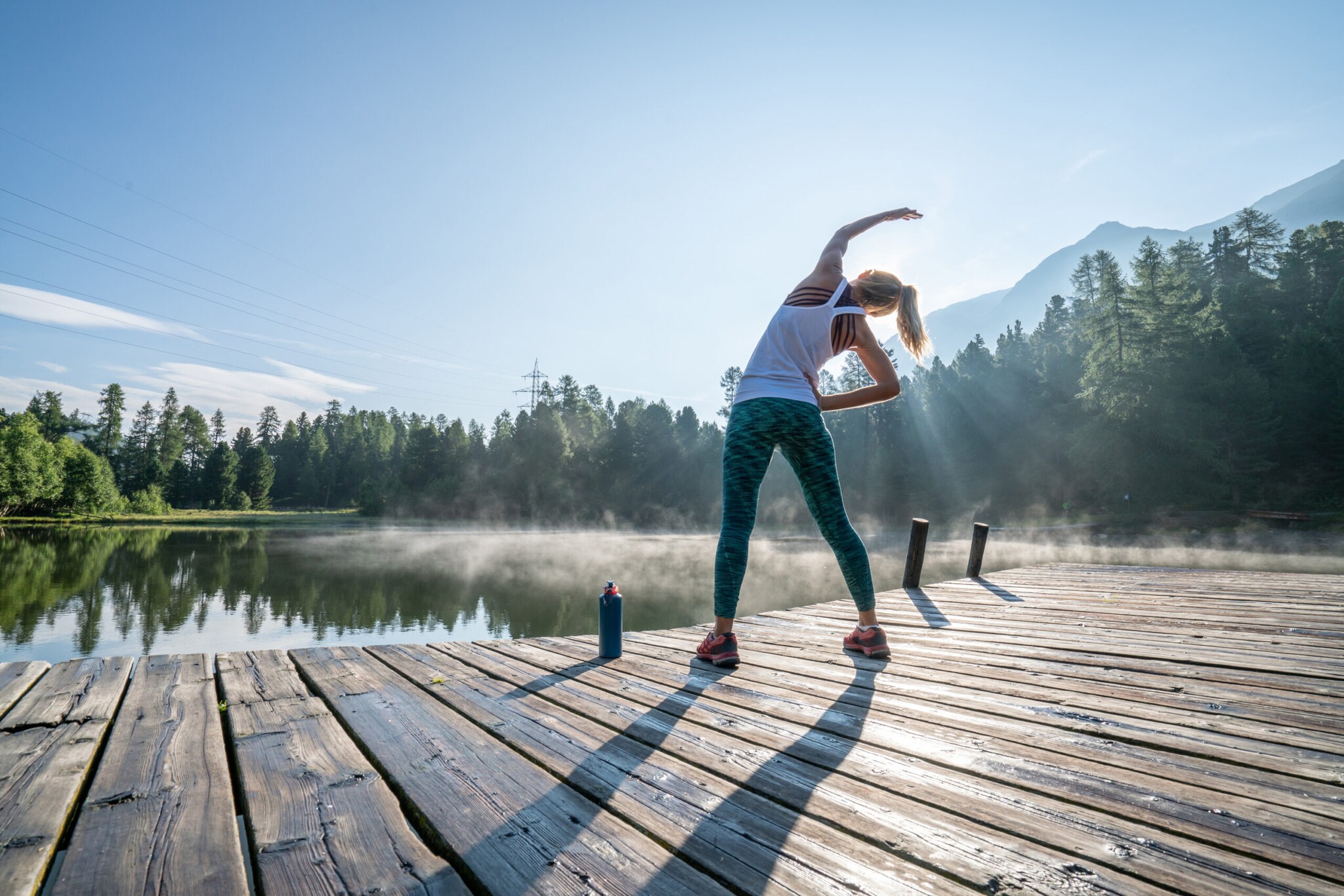 Eine junge Frau in Sportkleidung dehnt ihren Körper auf einem Holzsteg an einem See