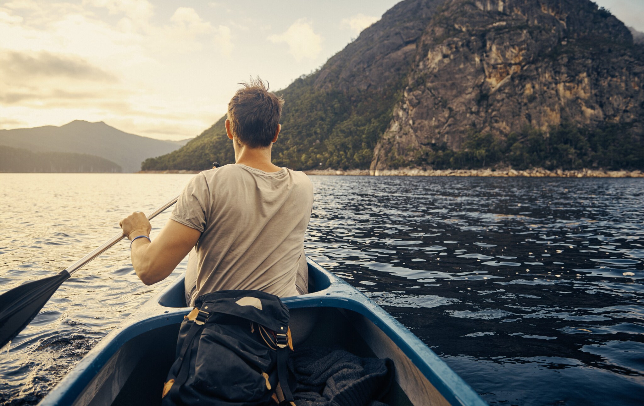 Mann paddelt auf einem Gewässer, im Hintergrund Berge