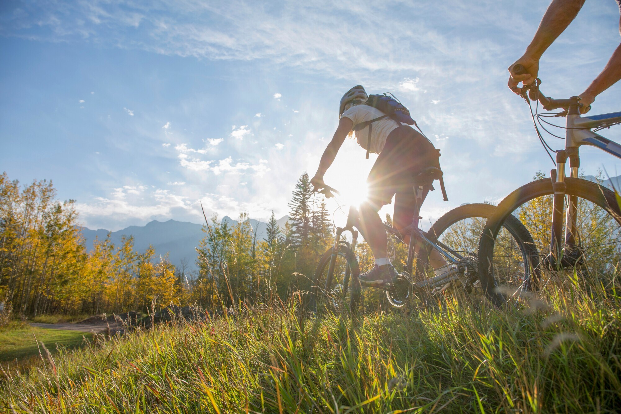 Zwei Radfahrer überqueren eine Wiese vor einem Bergpanorama Zwei Radfahrer überqueren eine Wiese vor einem Bergpanorama