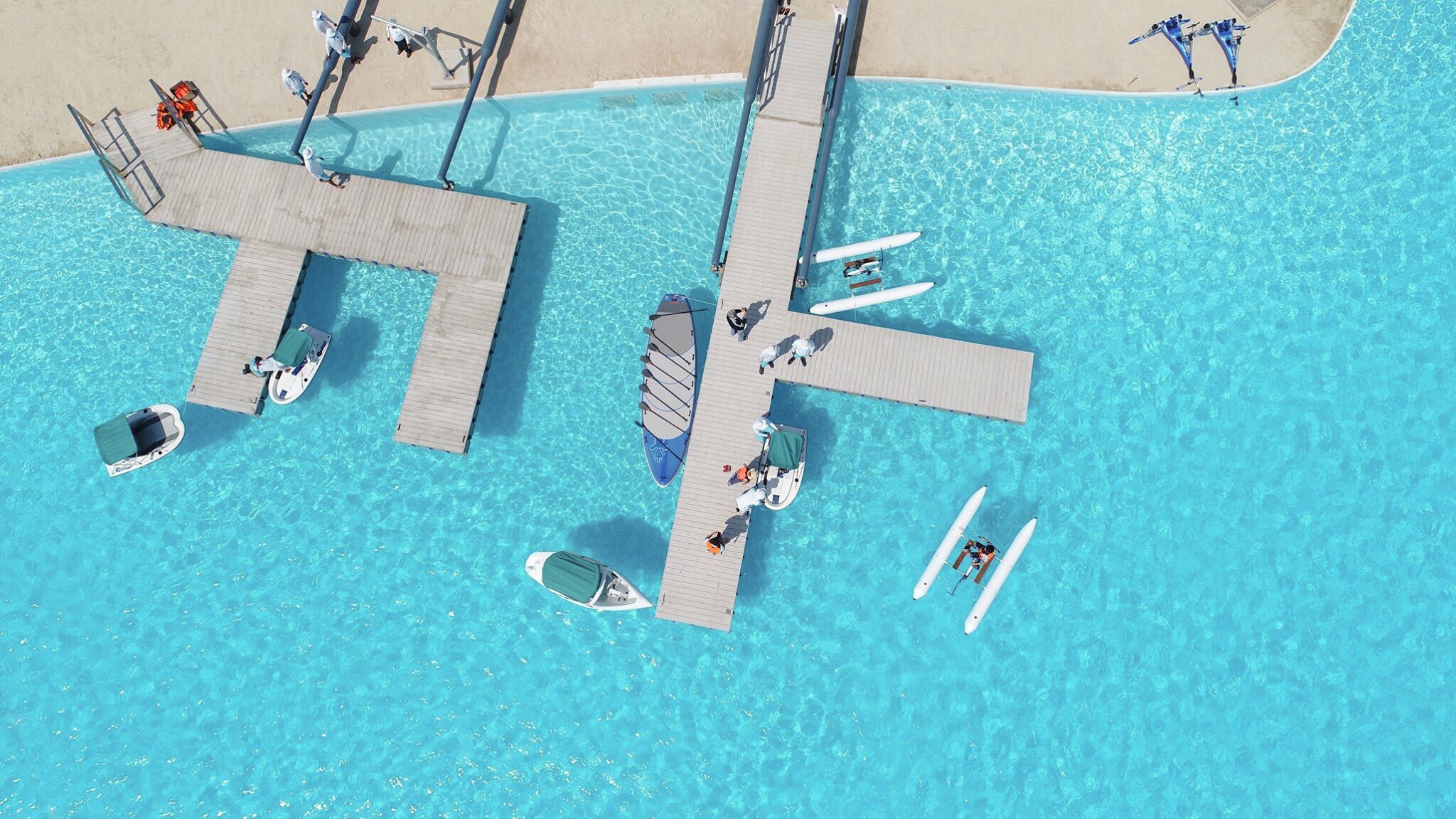 Ein großer Pool mit hellblauem, klaren Wasser sowie Booten, Katamaranen und zwei geometrischen hellgrauen Stegen in Betonoptik