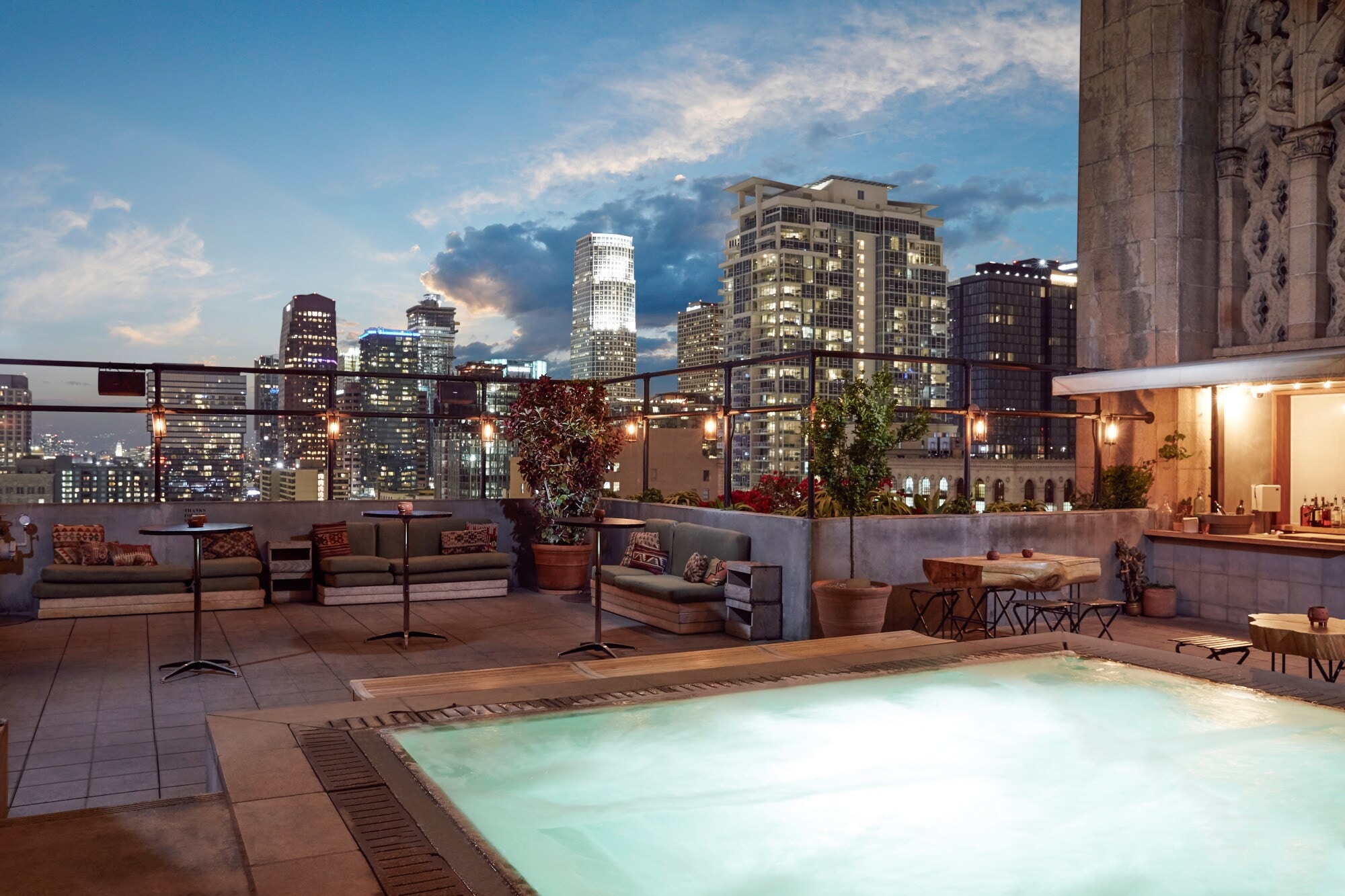 Dachterrasse mit Pool, Bar und Sitzmöglichkeiten mit Blick auf die Innenstadt von Los Angeles am Abend