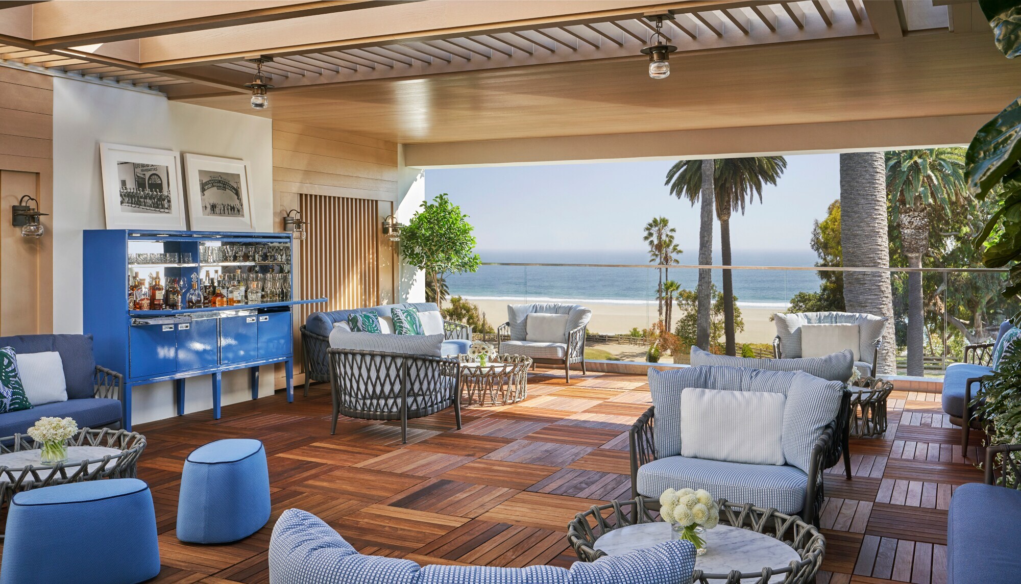 Überdachte Terrasse mit Holzboden und Polstermöbeln in Blautönen mit Blick auf Strand und Palmen Überdachte Terrasse mit Holzboden und Polstermöbeln in Blautönen mit Blick auf Strand und Palmen