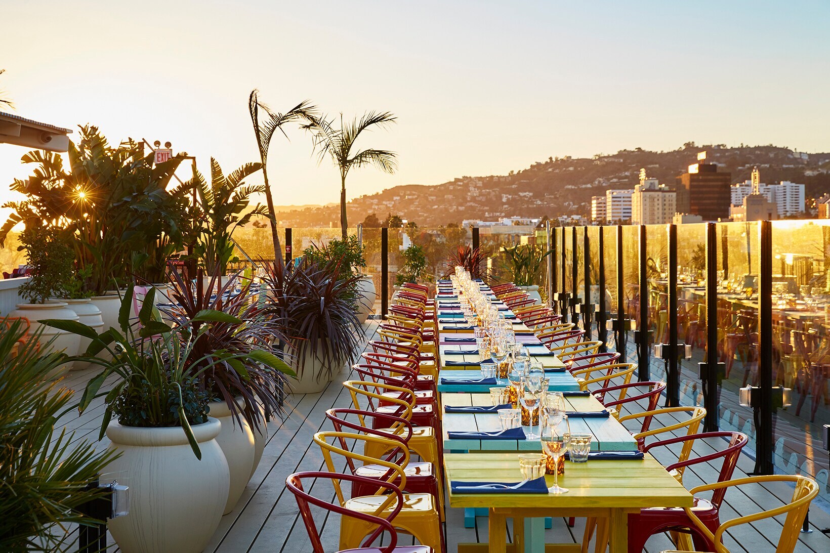 Dachterrasse mit Pflanzen und bunten, gedeckten Tischen im Sonnenuntergang Dachterrasse mit Pflanzen und bunten, gedeckten Tischen im Sonnenuntergang