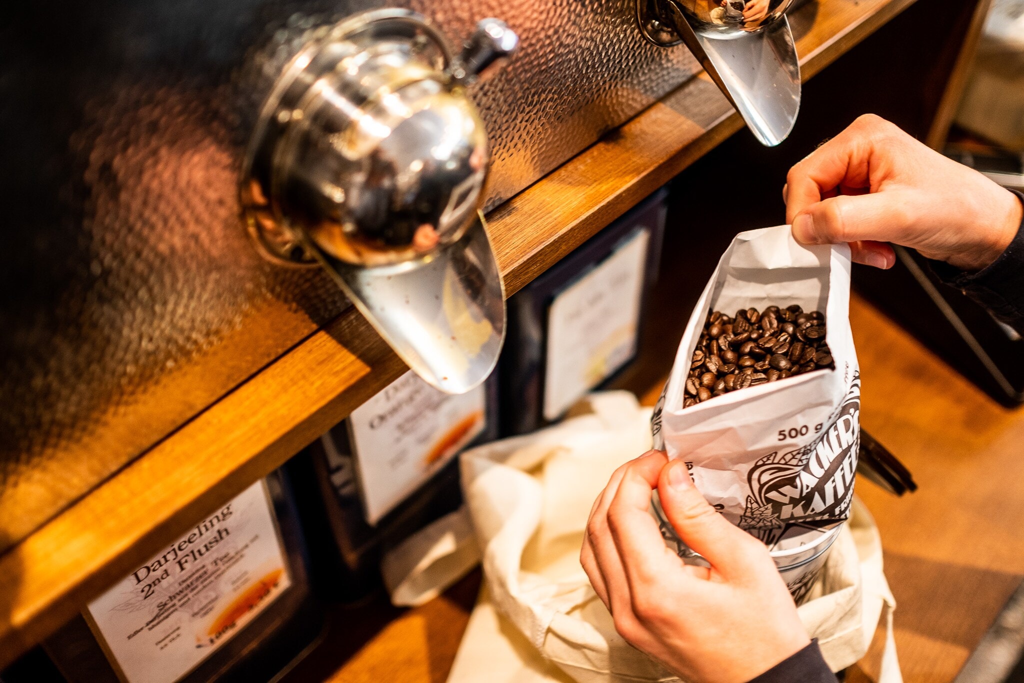 Nahaufnahme von zwei Händen, die in einem Geschäft einen Beutel mit Kaffeebohnen halten