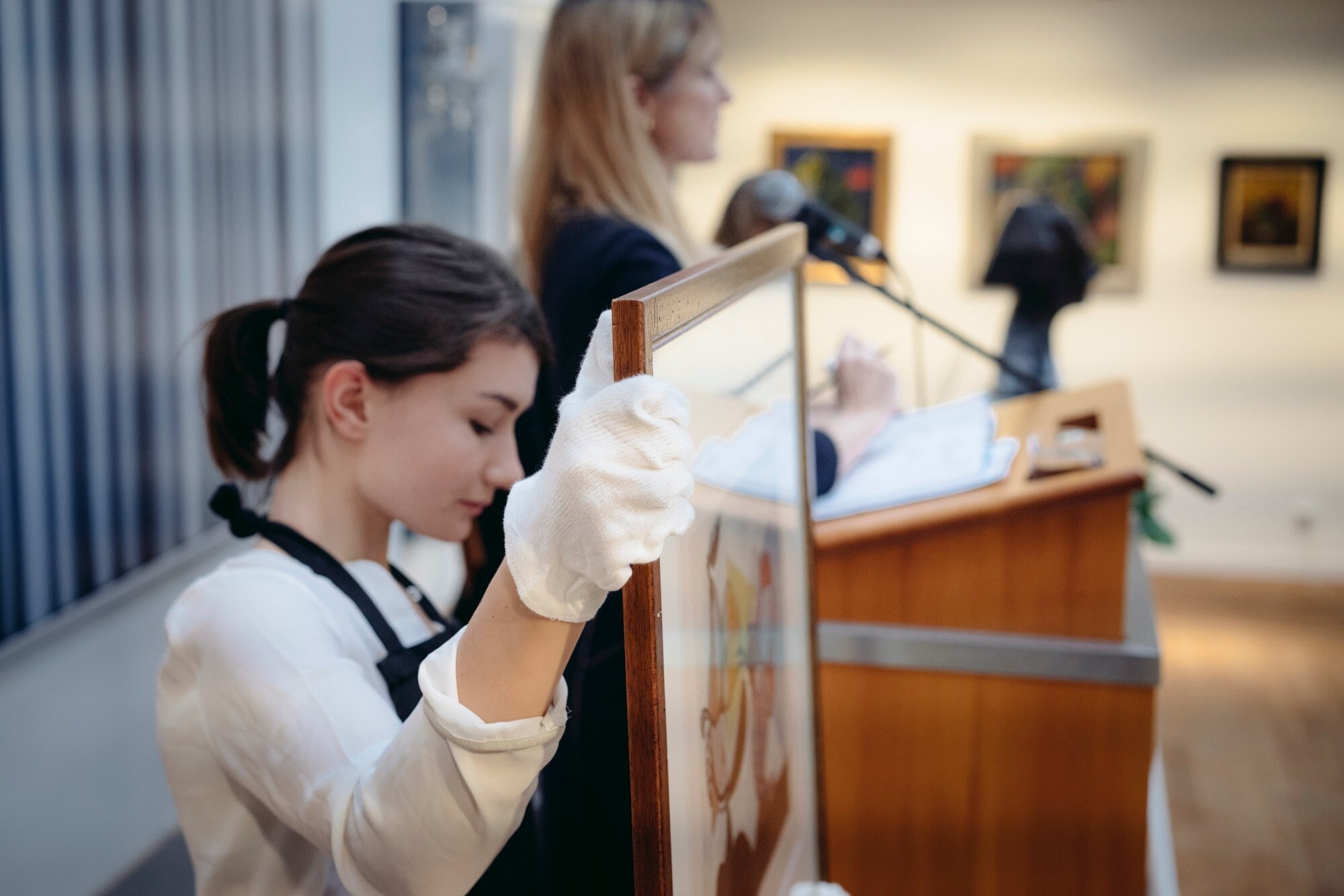 Eine Frau hält ein gerahmtes Bild während einer Auktion. Eine Frau hält ein gerahmtes Bild während einer Auktion.