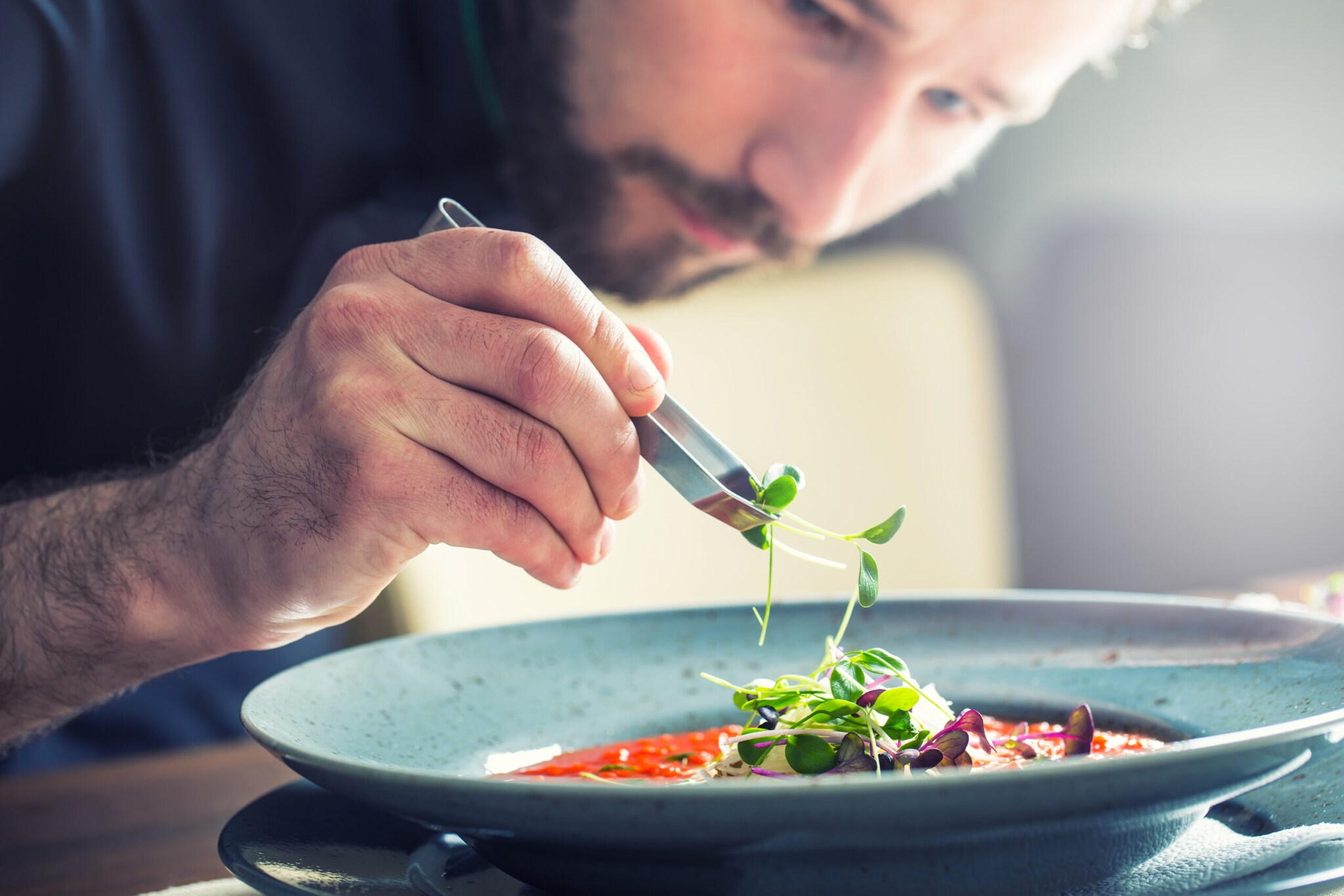 Ein Küchenchef richtet mit der Hand die Tomatensuppe an Ein Küchenchef richtet mit der Hand die Tomatensuppe an
