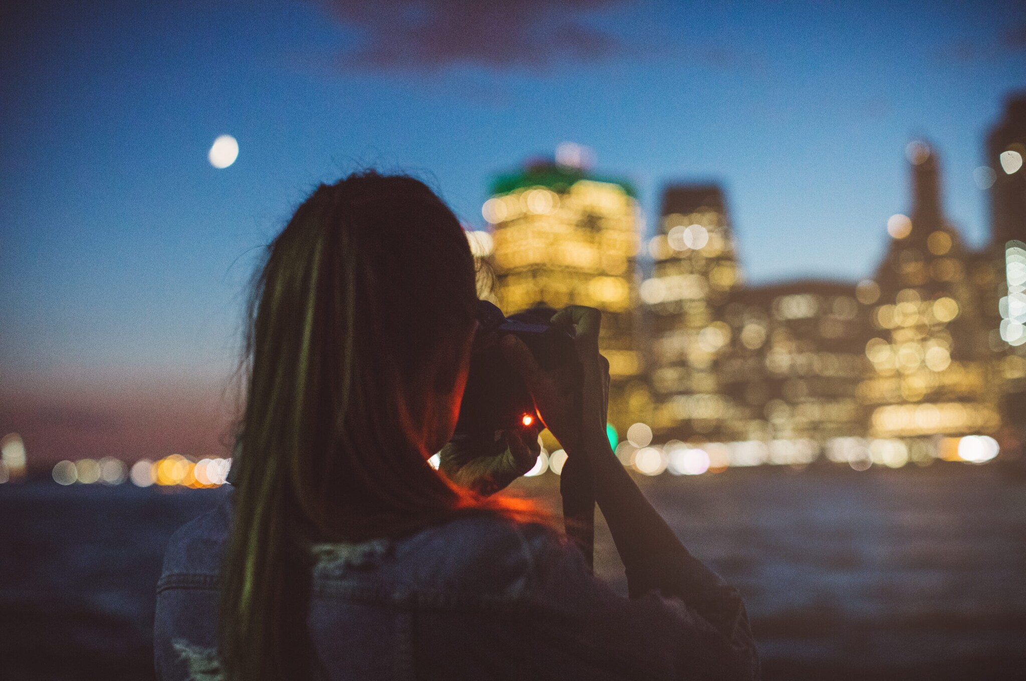 Eine Frau fotografiert in der Dämmerung eine beleuchtete Häuserzeile